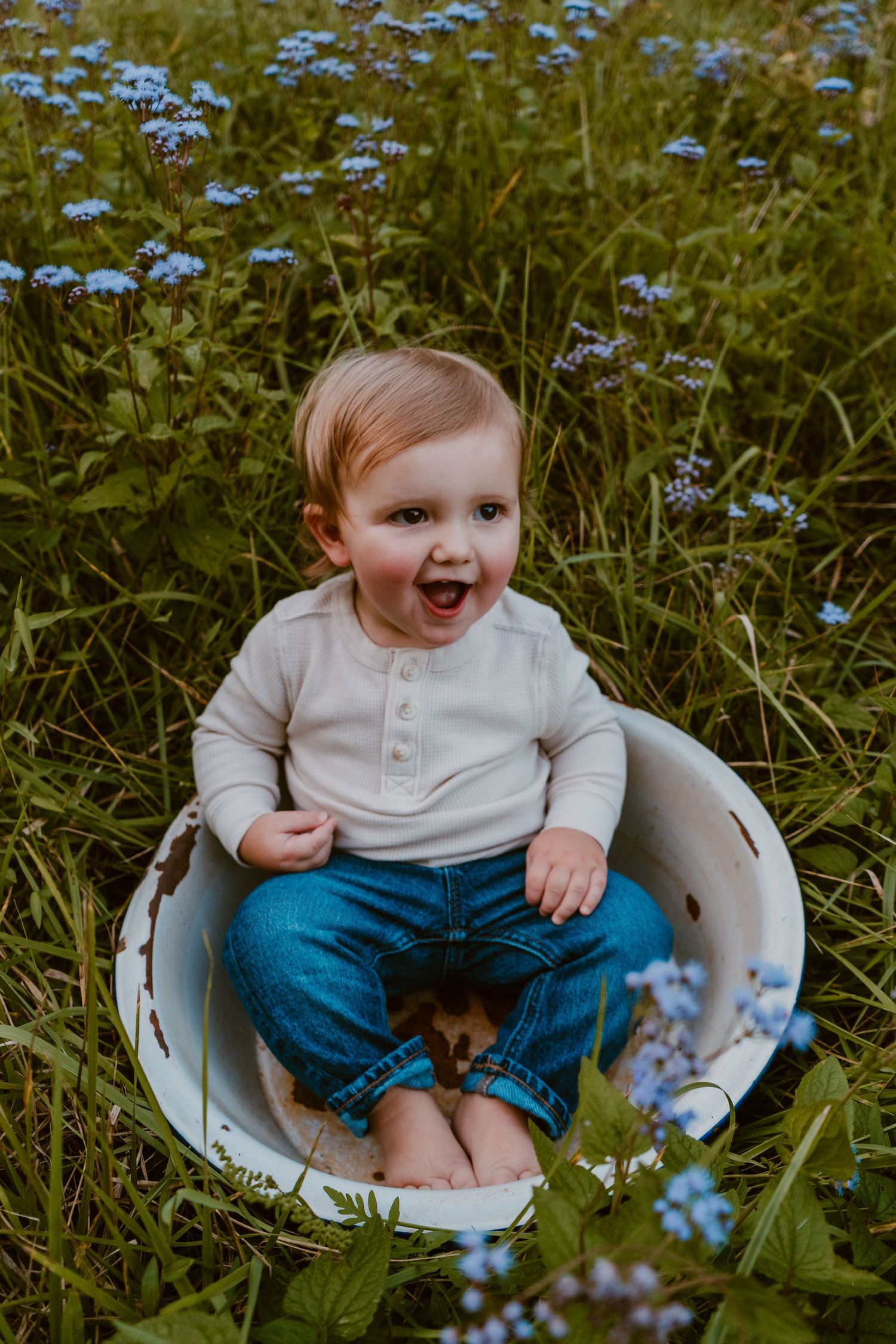 Baby sits in white basin surrounded by blooming blue wildflowers.