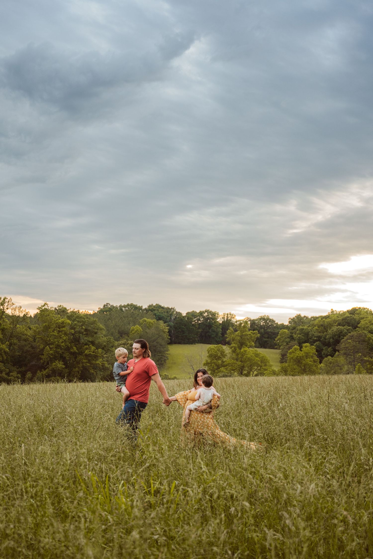 Family running and playing together in a tall grass field at dusk.