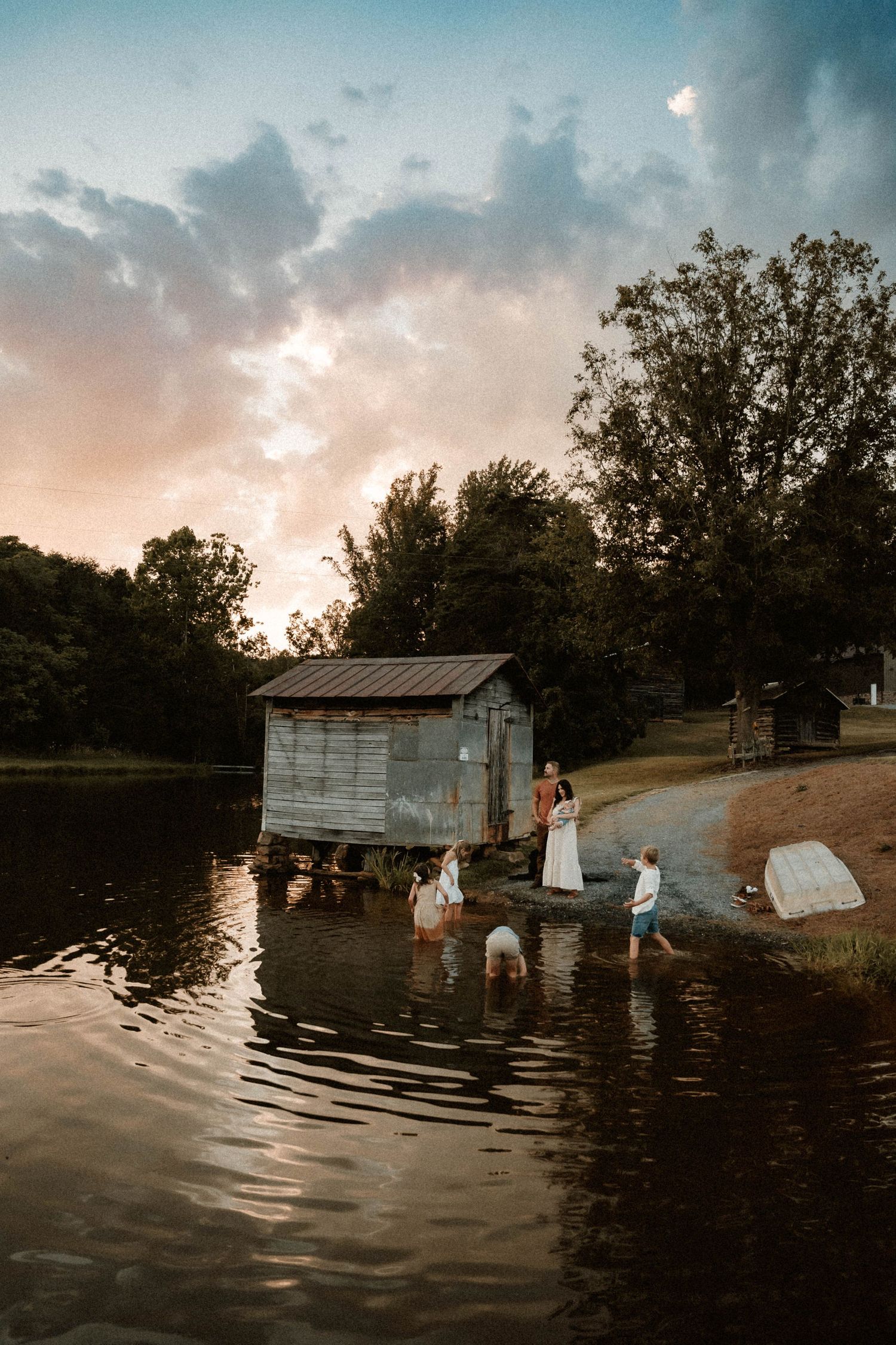 A group wades in a tranquil lake at sunset near a rustic wooden structure.