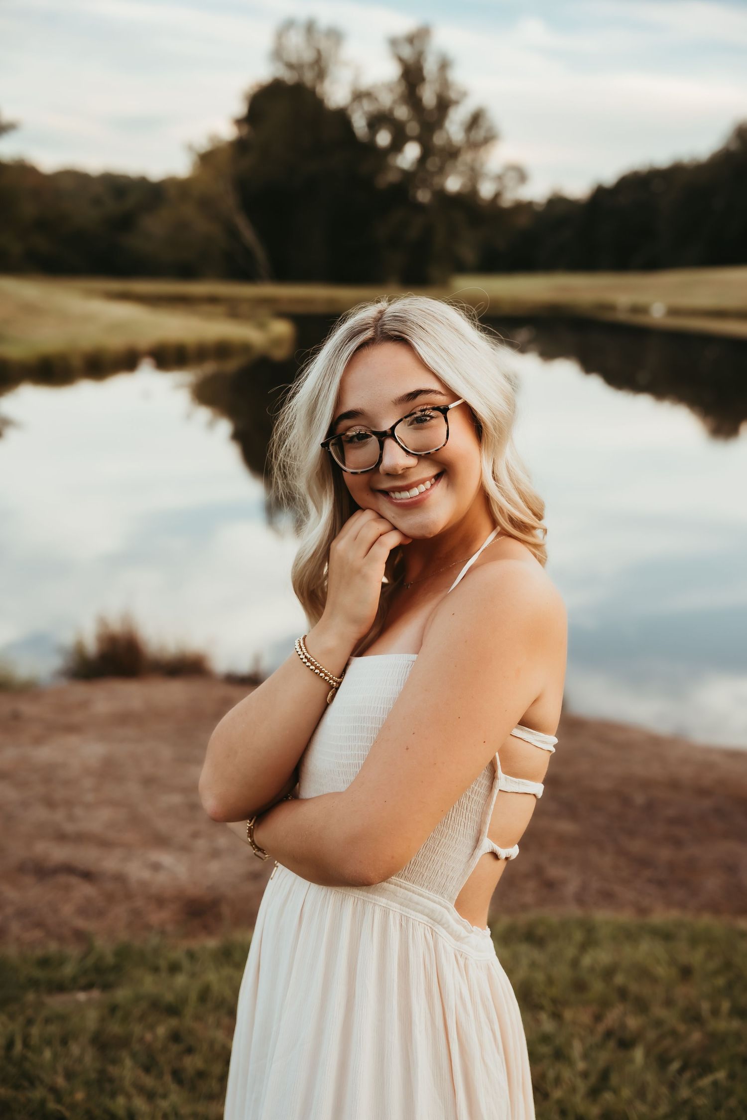 Woman in white dress poses by lakeside during sunset photoshoot.