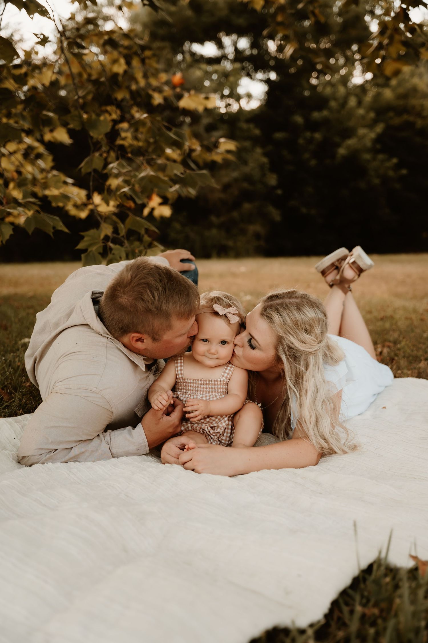 A family shares intimate moments while lying on a white blanket outdoors.