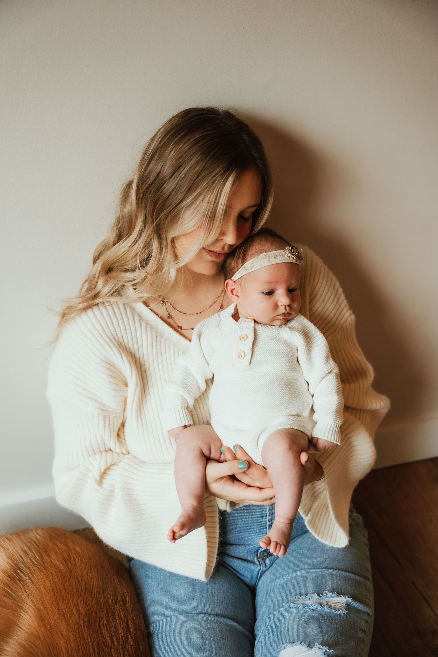Mother and baby sharing tender moments in cozy white sweaters and jeans against neutral background.