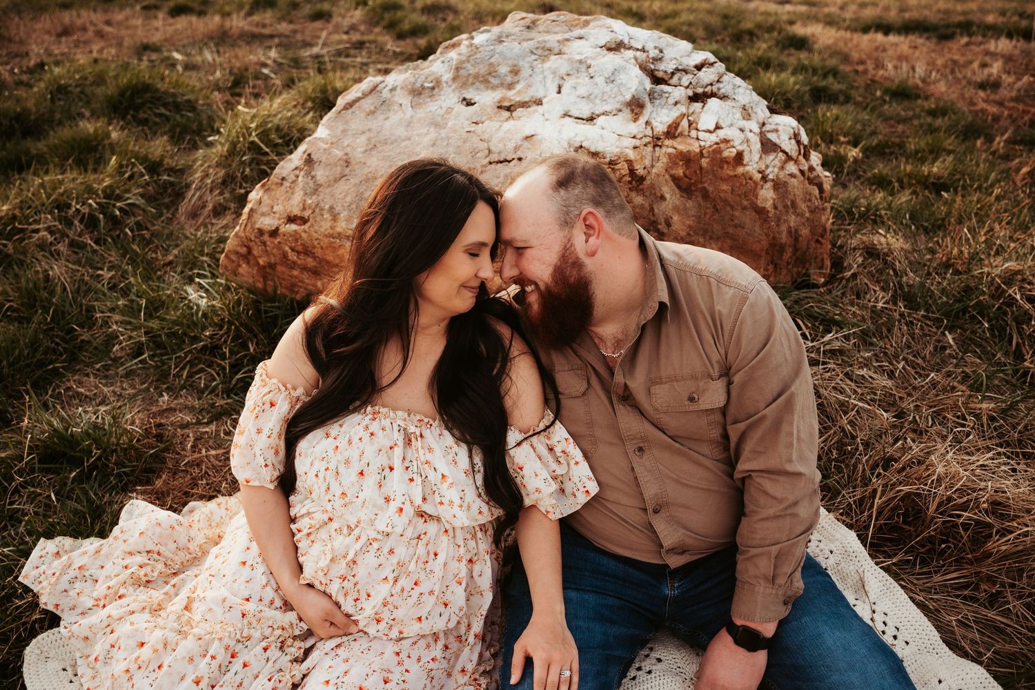 Intimate moment between couple sitting on blanket against rocky backdrop at sunset.