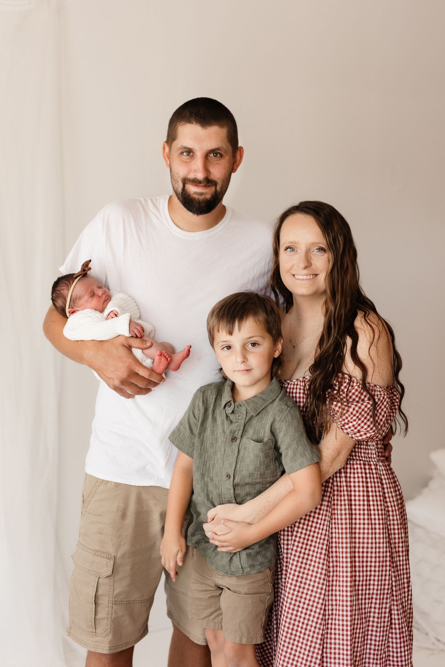 Family portrait session against neutral background in coordinated casual outfits.
