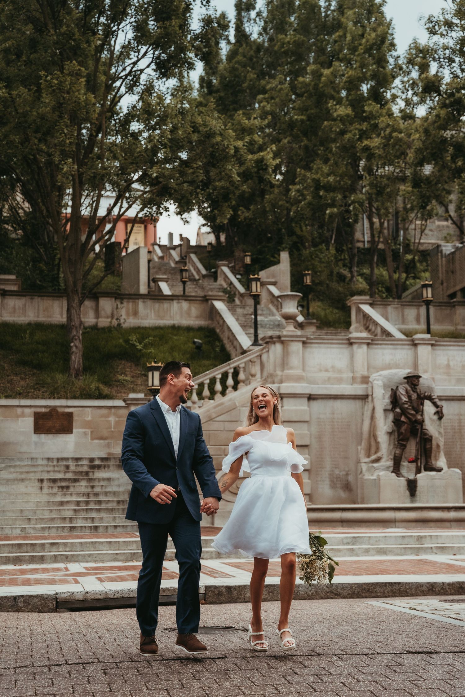 Wedding couple poses playfully on stone steps of an elegant architectural setting.