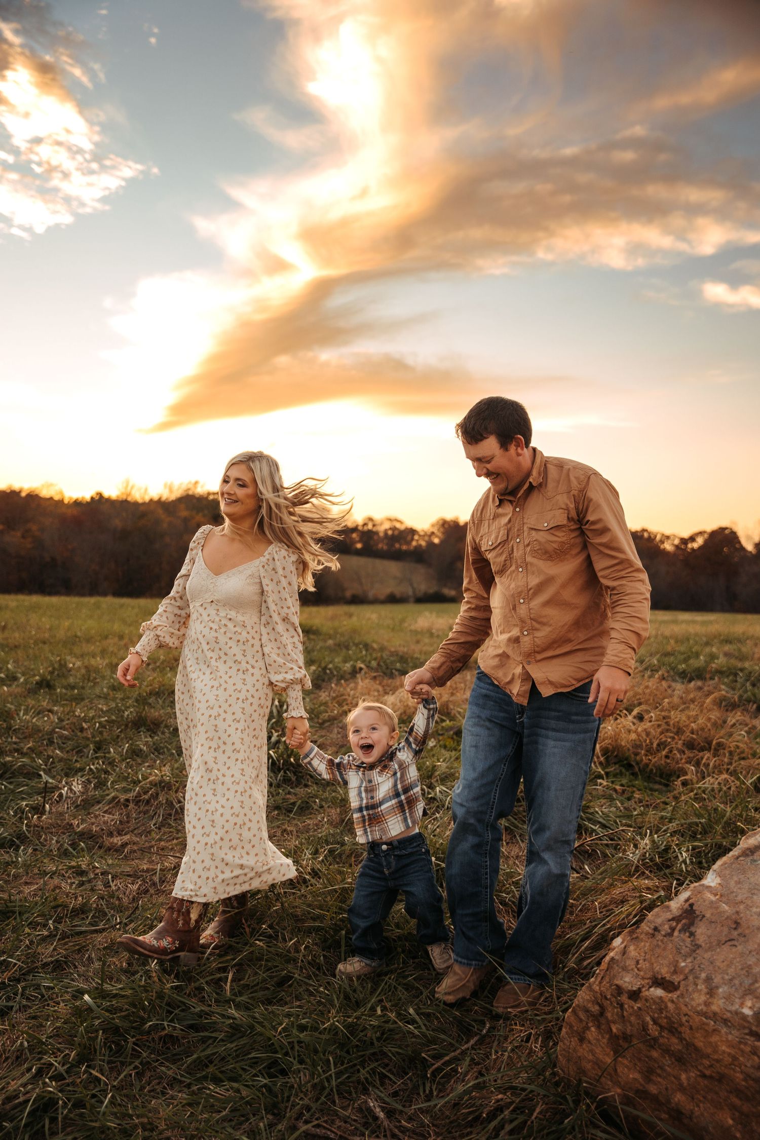 Family walks together through a golden field at sunset.