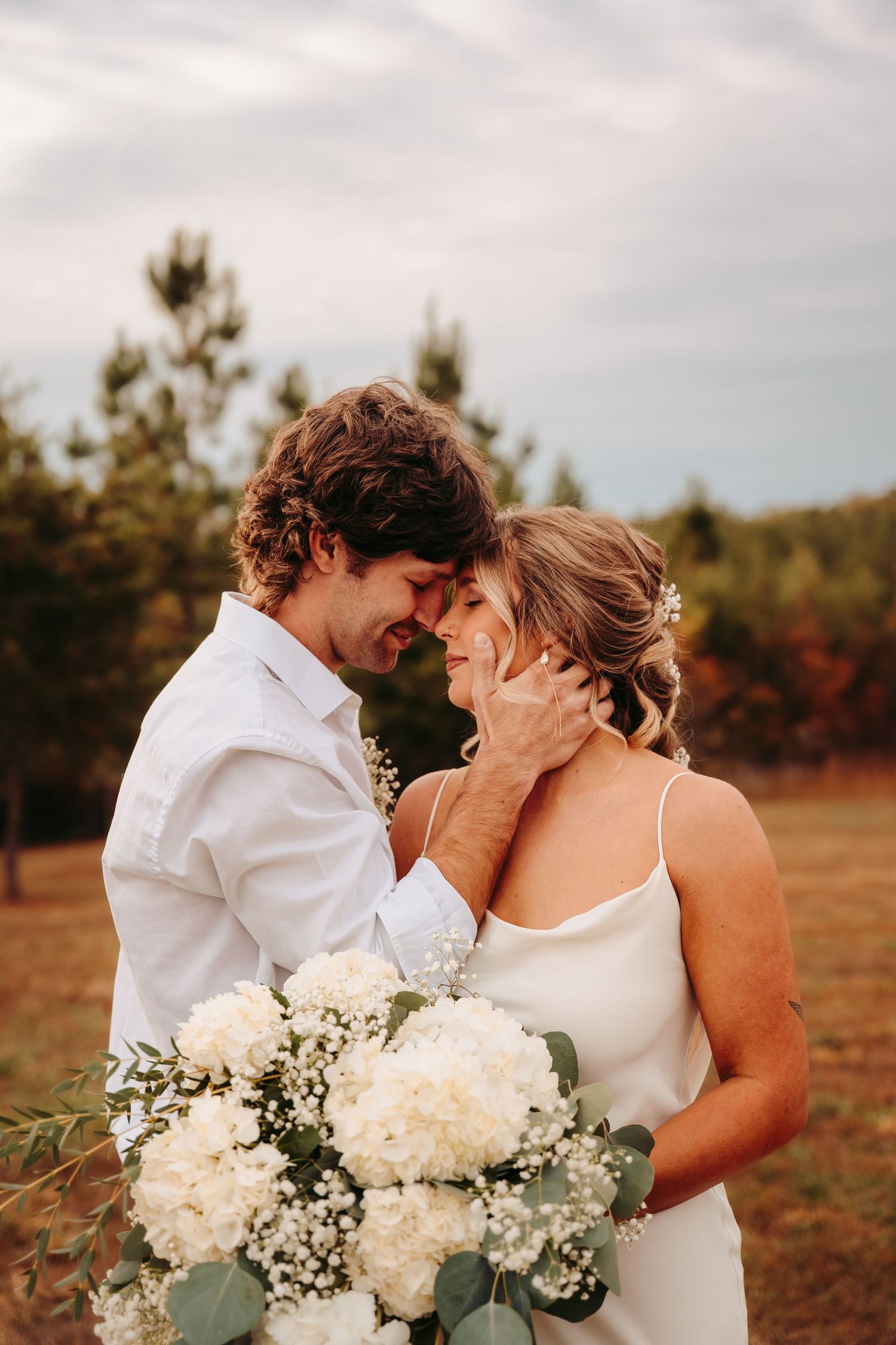 Intimate wedding couple moment with white bouquet in autumn field.