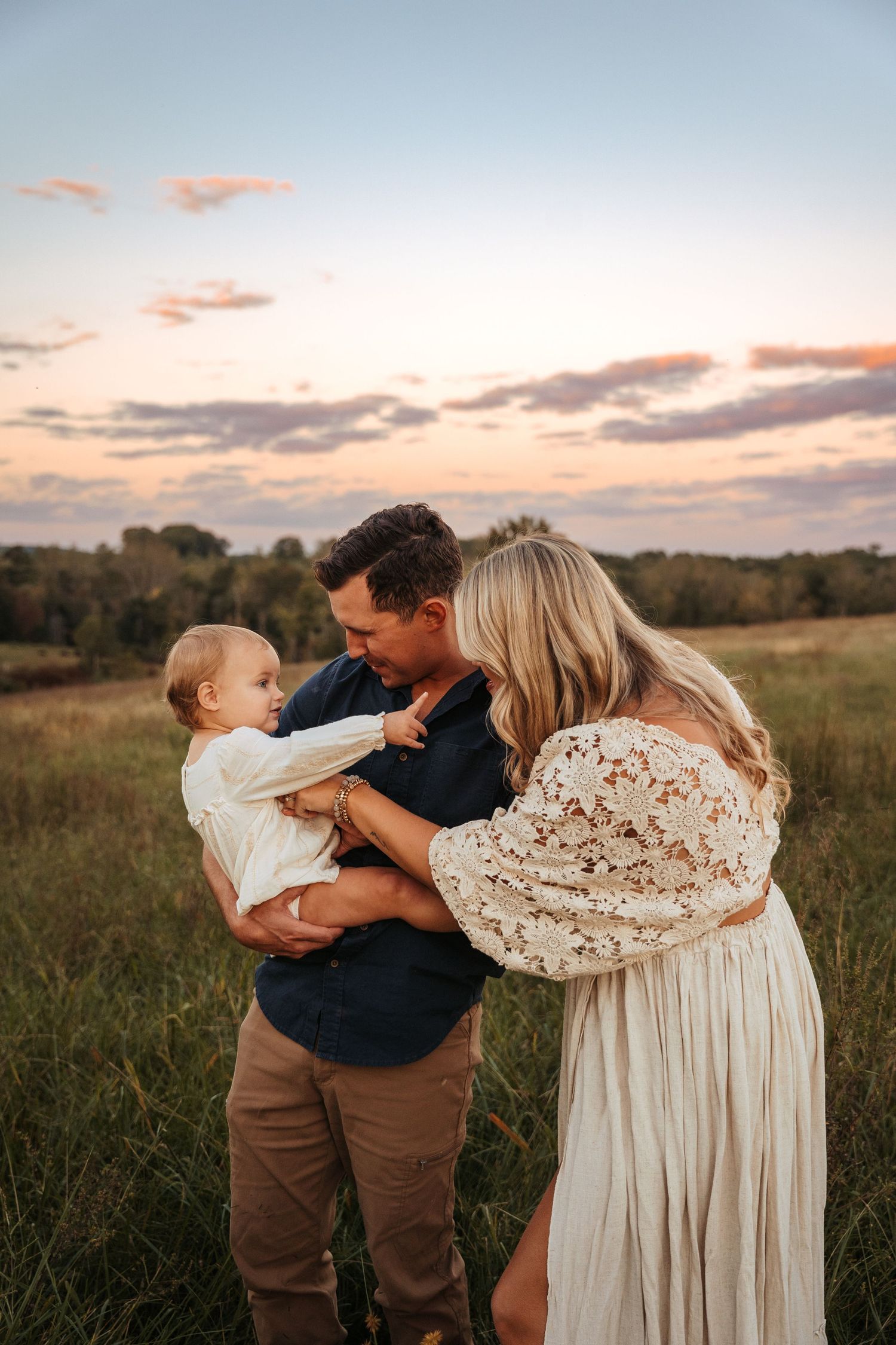 Family shares tender moments in a field during sunset.