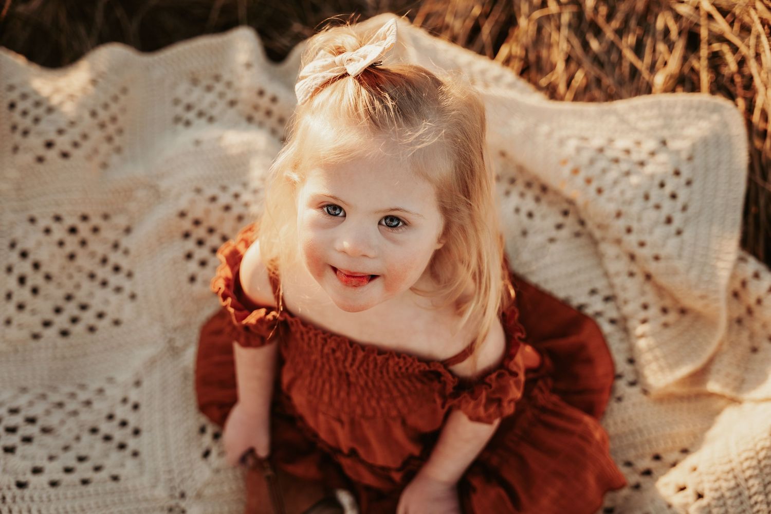 Baby in rust-colored dress lying on white lace blanket.