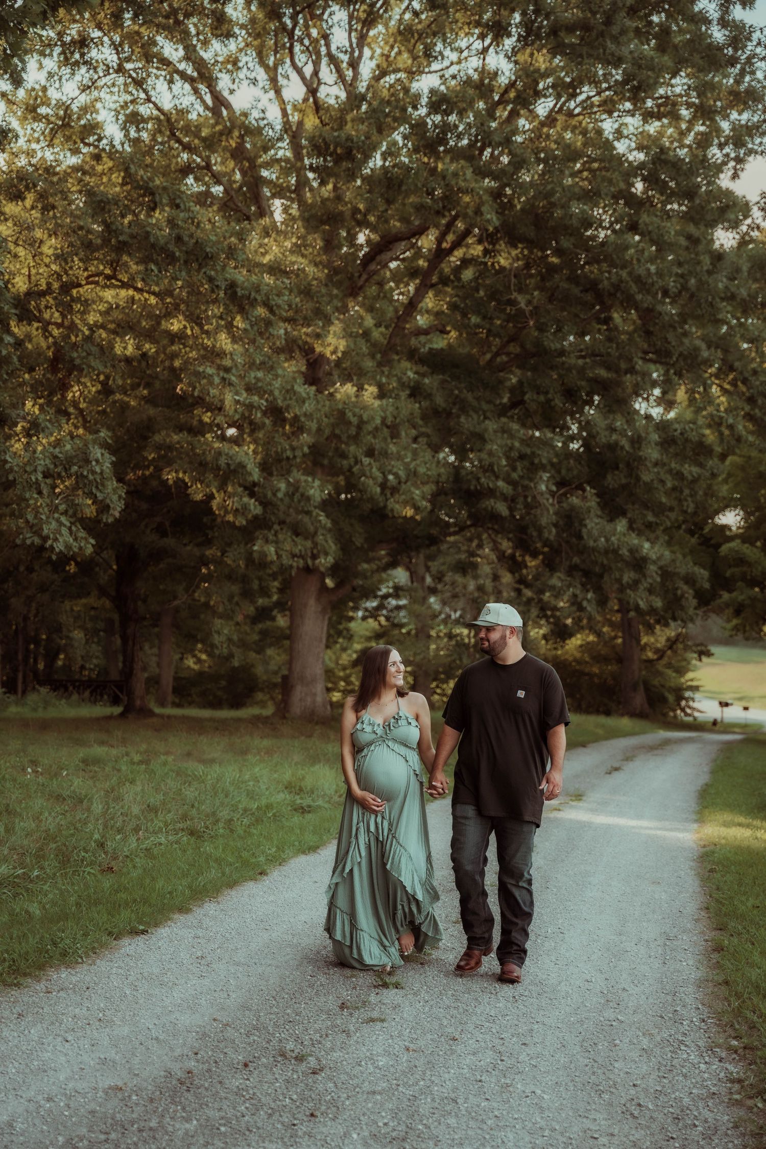 Couple walks together on gravel path through wooded park at sunset.