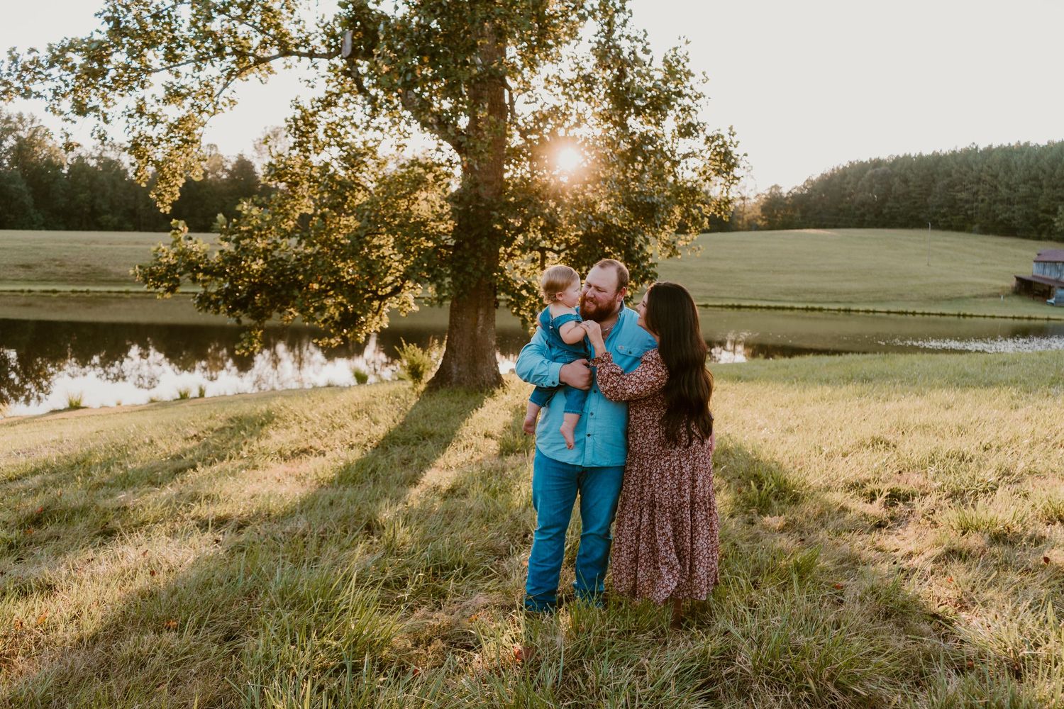 Family standing together in a meadow with trees and golden sunlight.