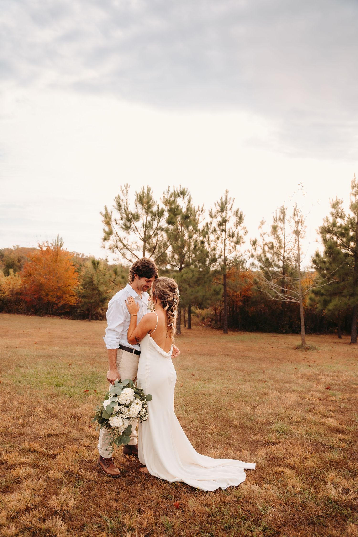 Romantic wedding couple poses in field during golden hour.
