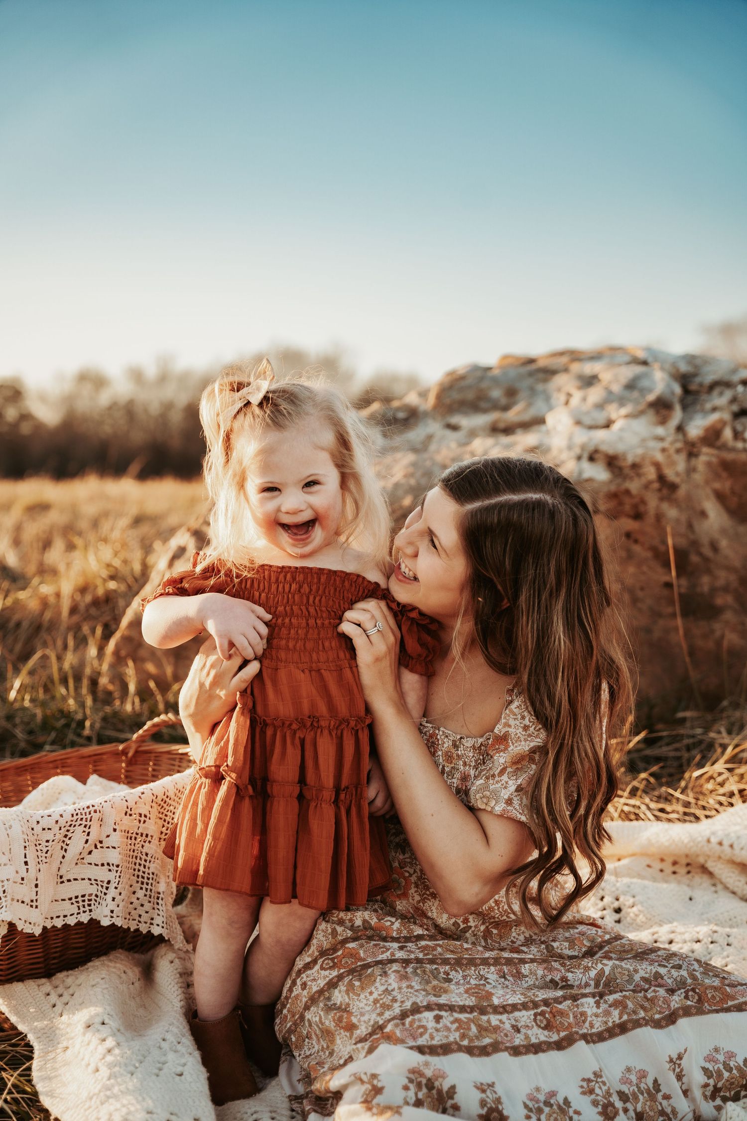 Two children share joyful moments on a blanket during golden hour.