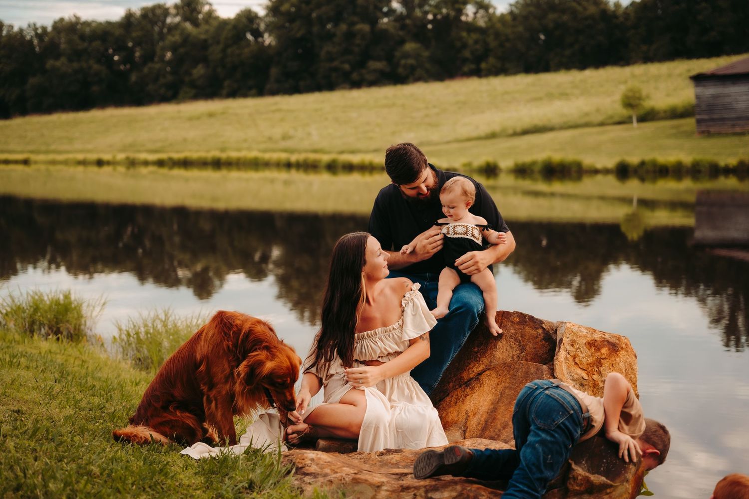 A couple relaxes by a serene pond during sunset in a pastoral setting.