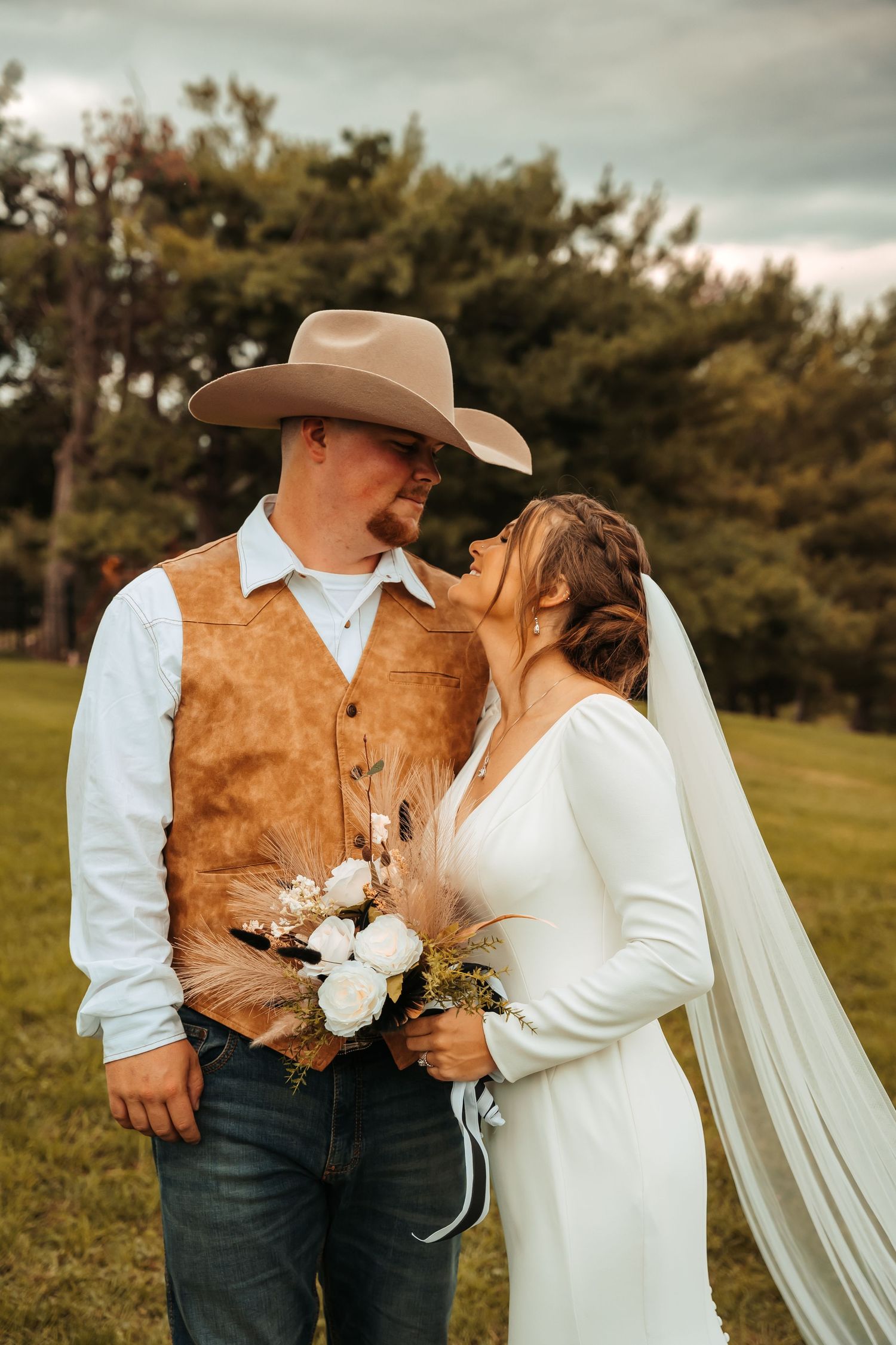 Wedding couple in country western attire posing in grassy field.