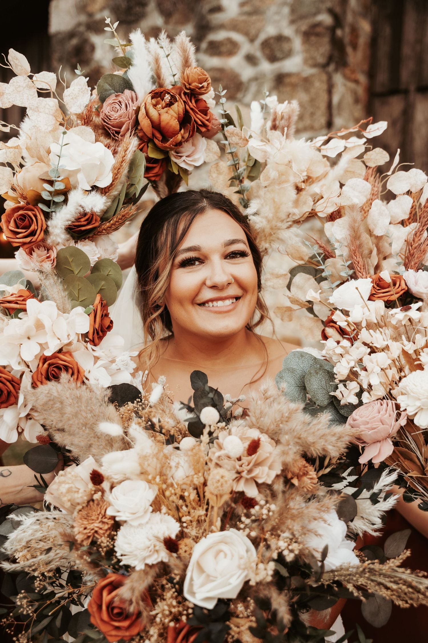 Bridal portrait surrounded by autumn-toned floral arrangement with roses and dried flowers.