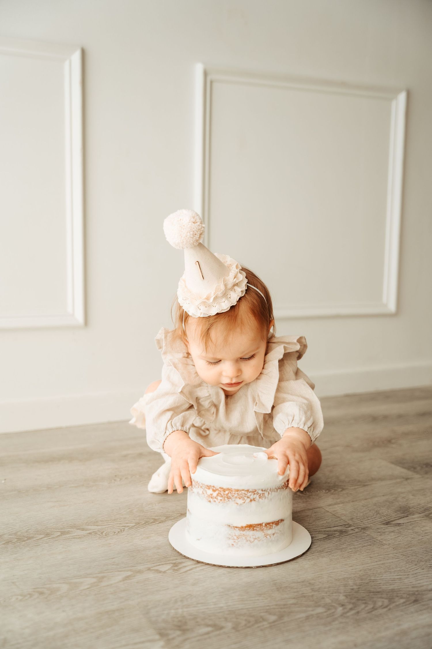 Baby in white dress exploring cake during first birthday cake smash photo session.