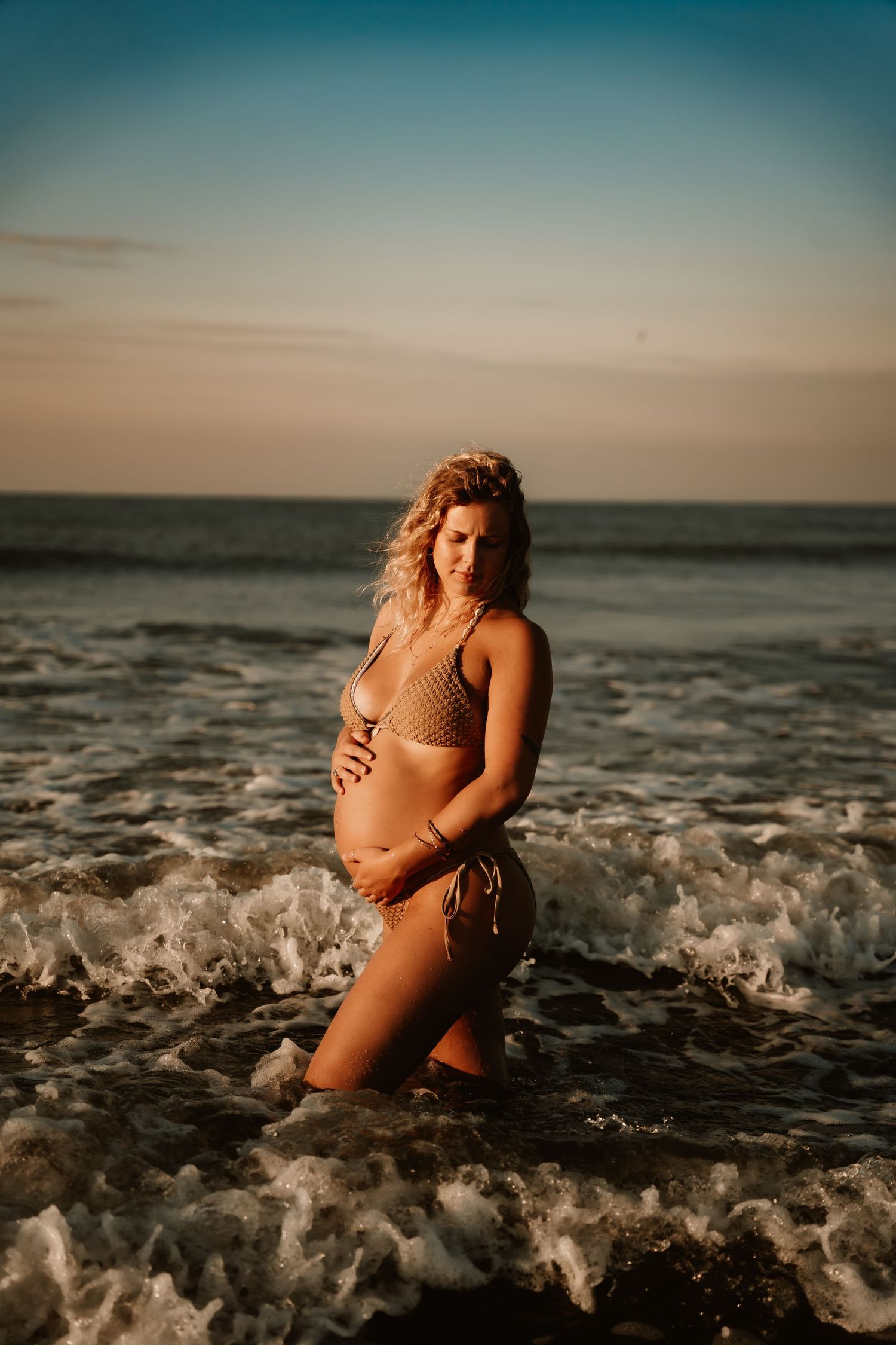 Woman enjoys ocean waves during sunset beach photoshoot.