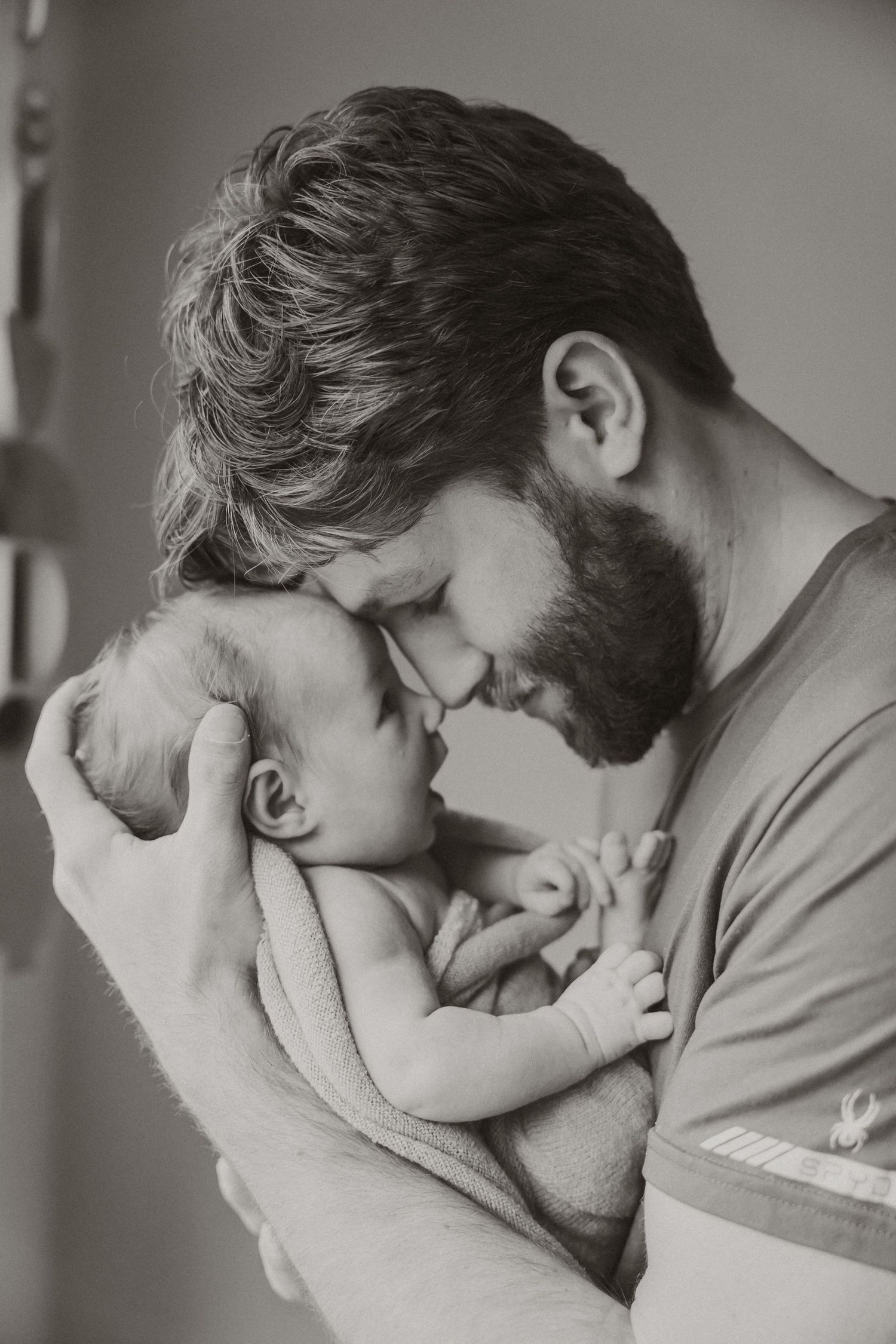 Tender moment between parent and newborn in black and white portrait.