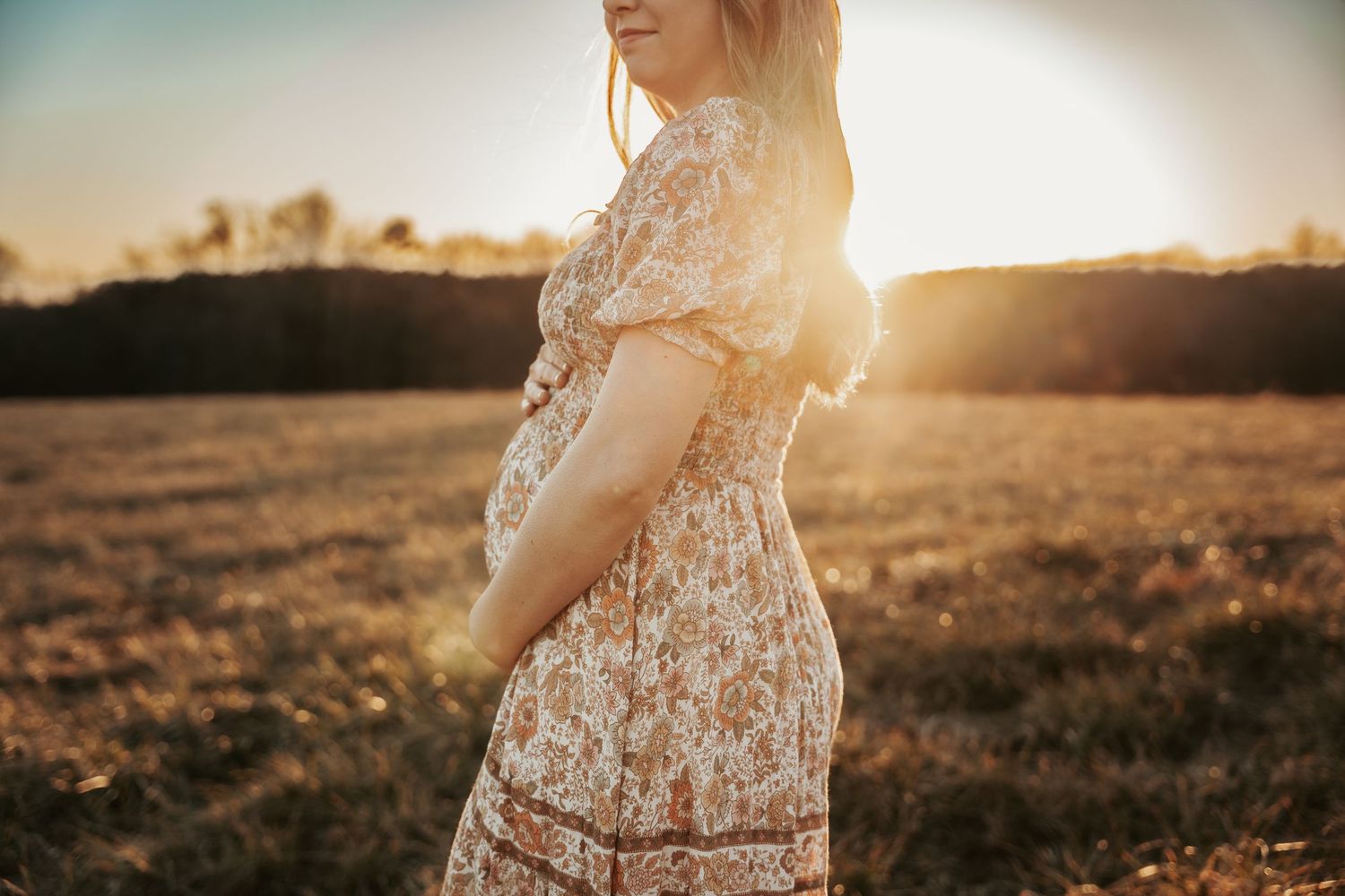 Woman in floral dress poses gracefully in a sunlit meadow.