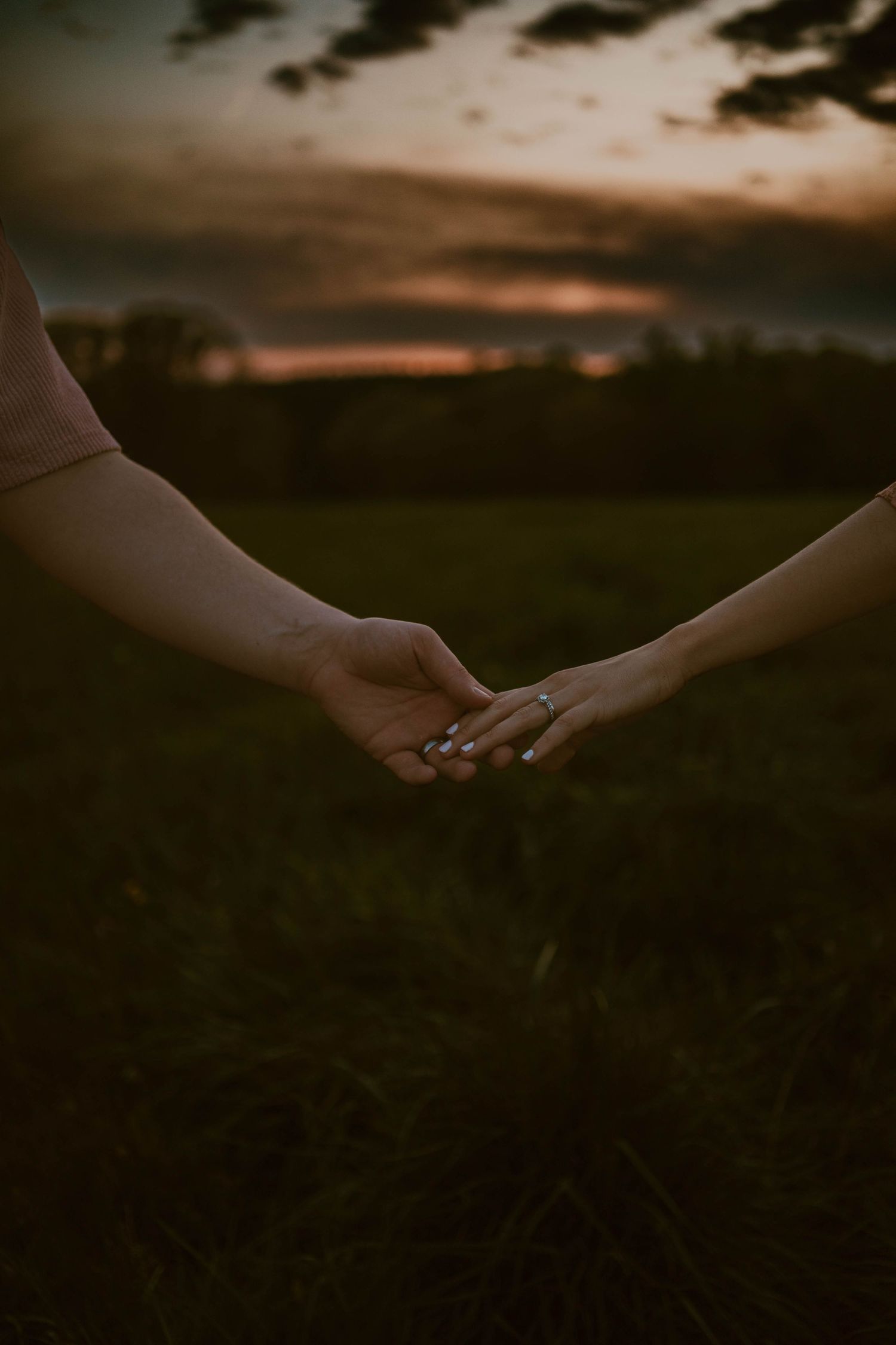 Close-up of hands reaching toward each other in a field at sunset.