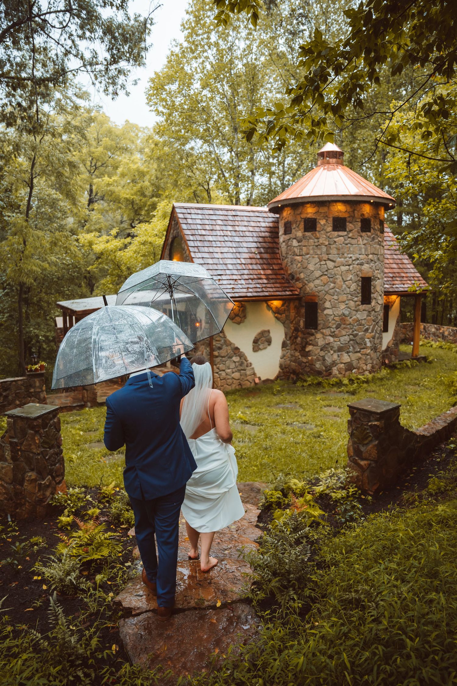 People walking with umbrellas in the rain near stone cottages.