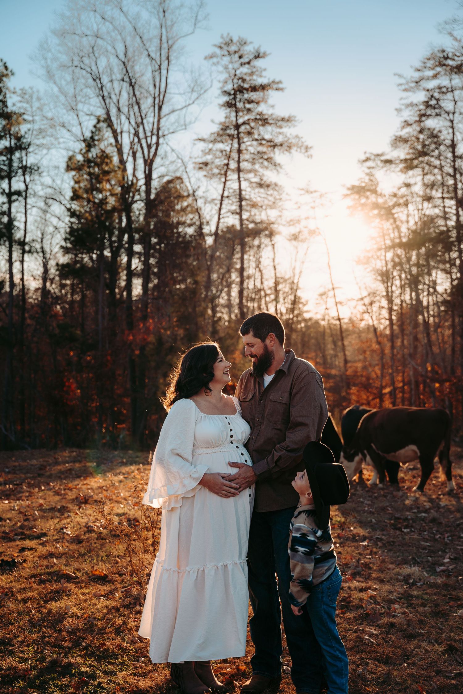 Sunset family portrait session in a wooded area with golden light filtering through bare trees.