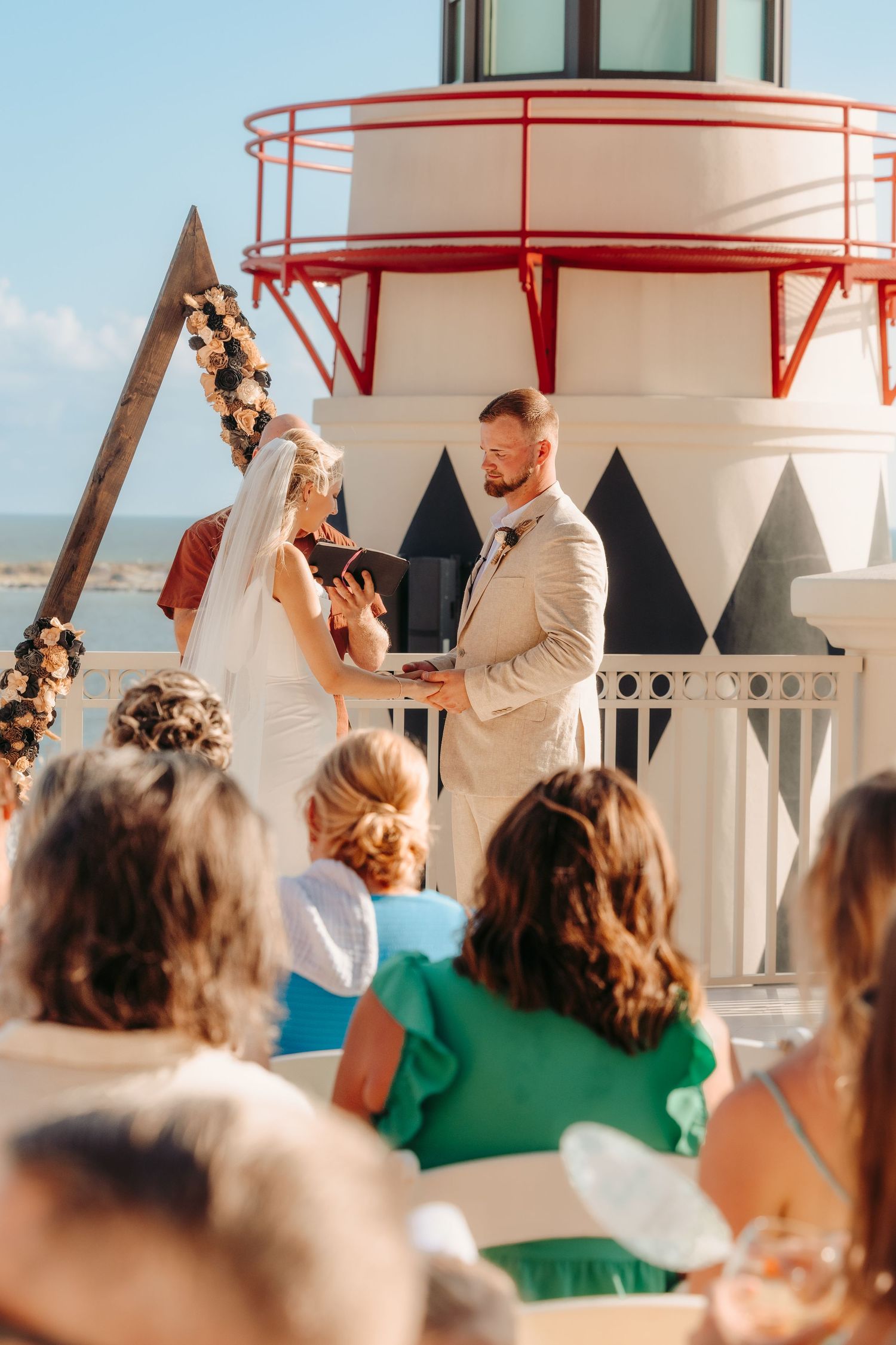 Wedding celebration at a coastal lighthouse venue with guests gathered under a red railing.