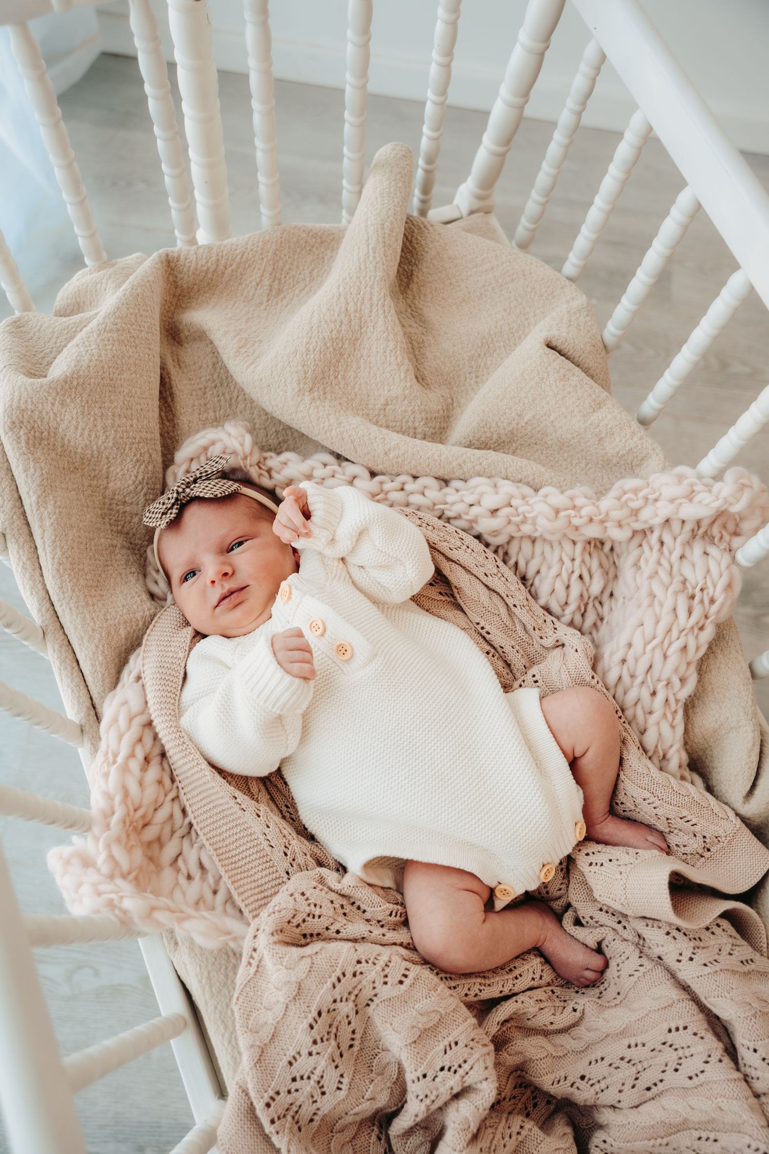 Newborn baby sleeping peacefully on knit blanket in white rocking chair.