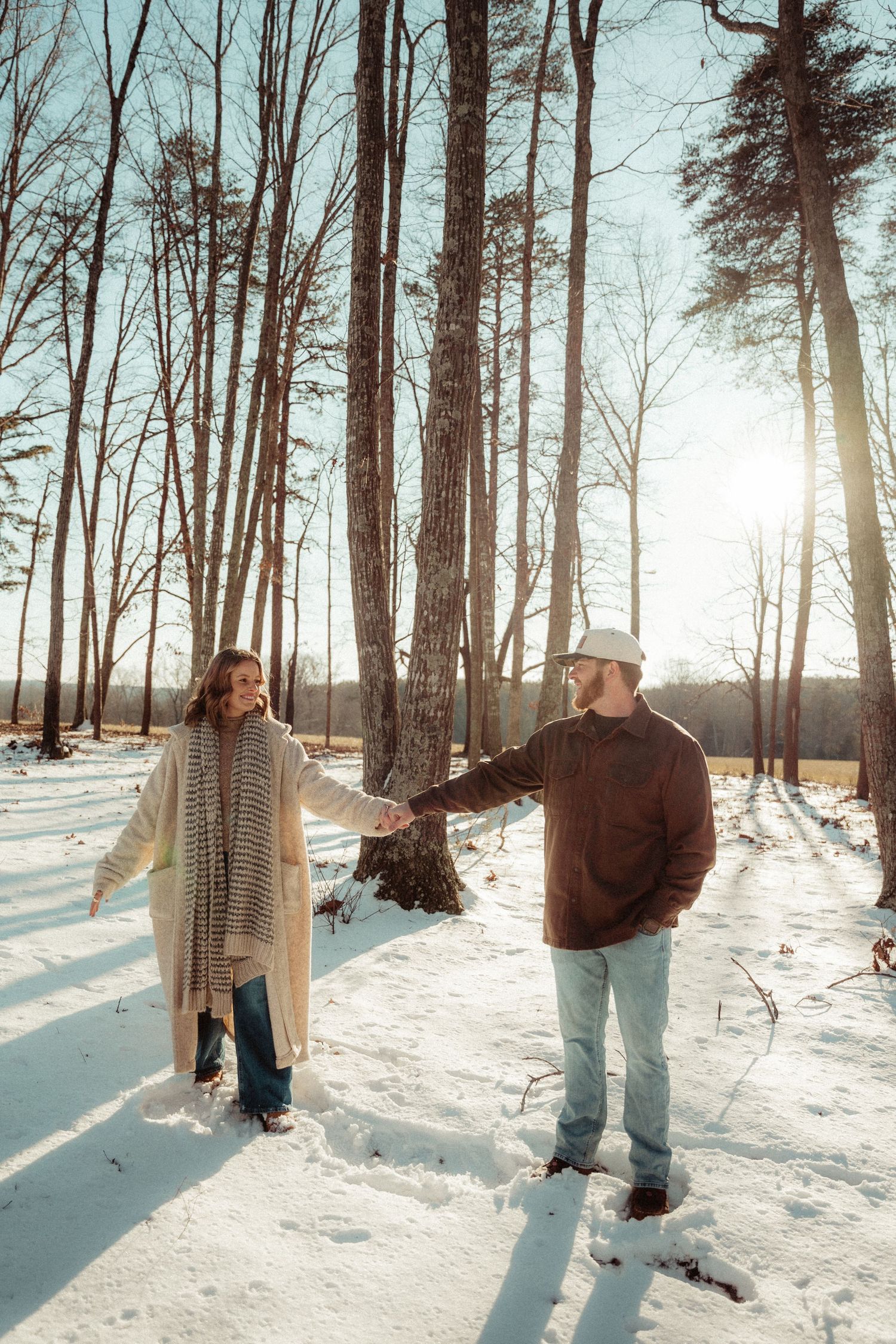 A couple enjoying a winter walk through tall snow-covered trees in a forest.