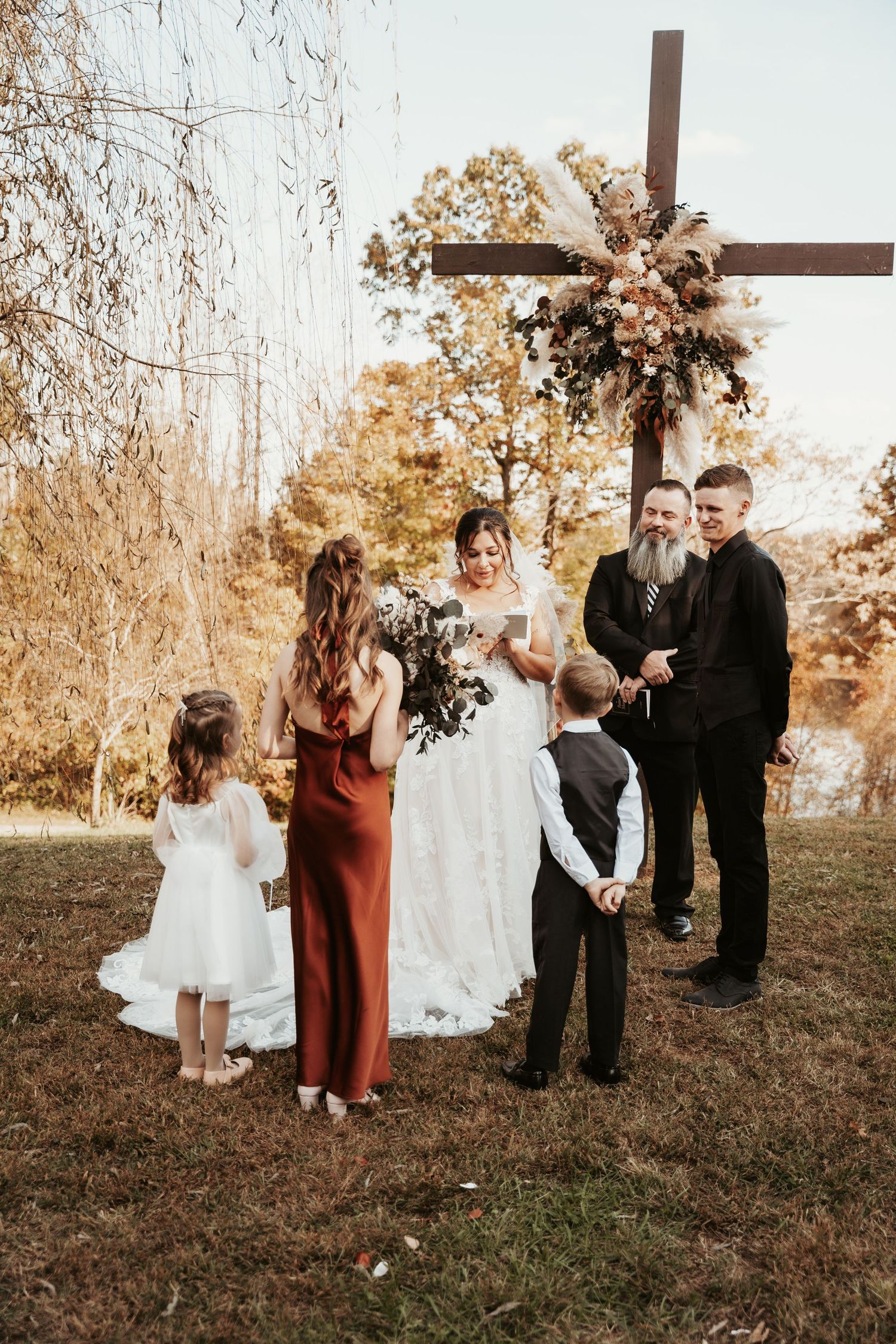 Wedding ceremony gathering under decorated wooden cross in autumn setting.