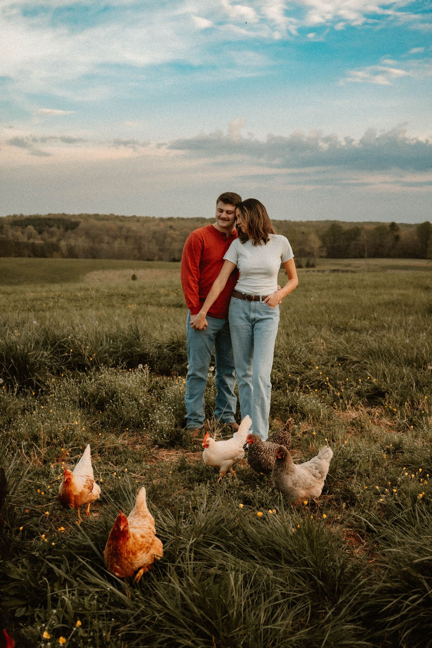 A casual outdoor photoshoot in a field with chickens roaming in the foreground.