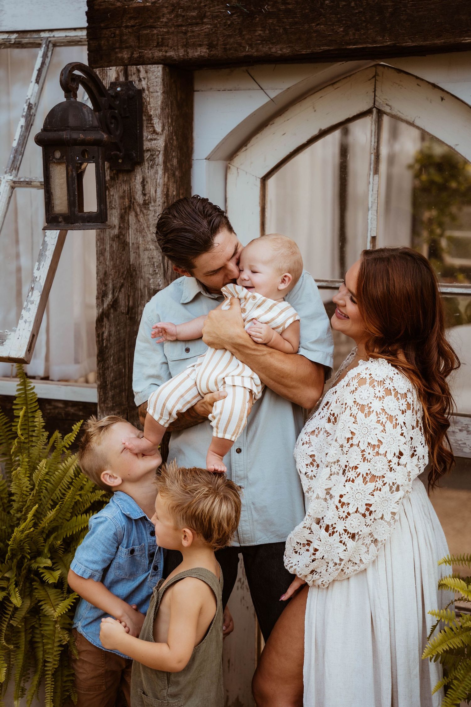 A joyful family moment shared outside a rustic doorway with ferns and a vintage lantern.