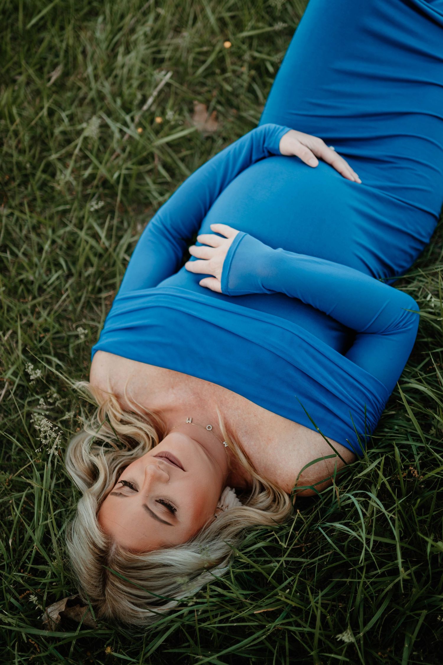 An artistic maternity portrait in a bright blue dress against natural grass.