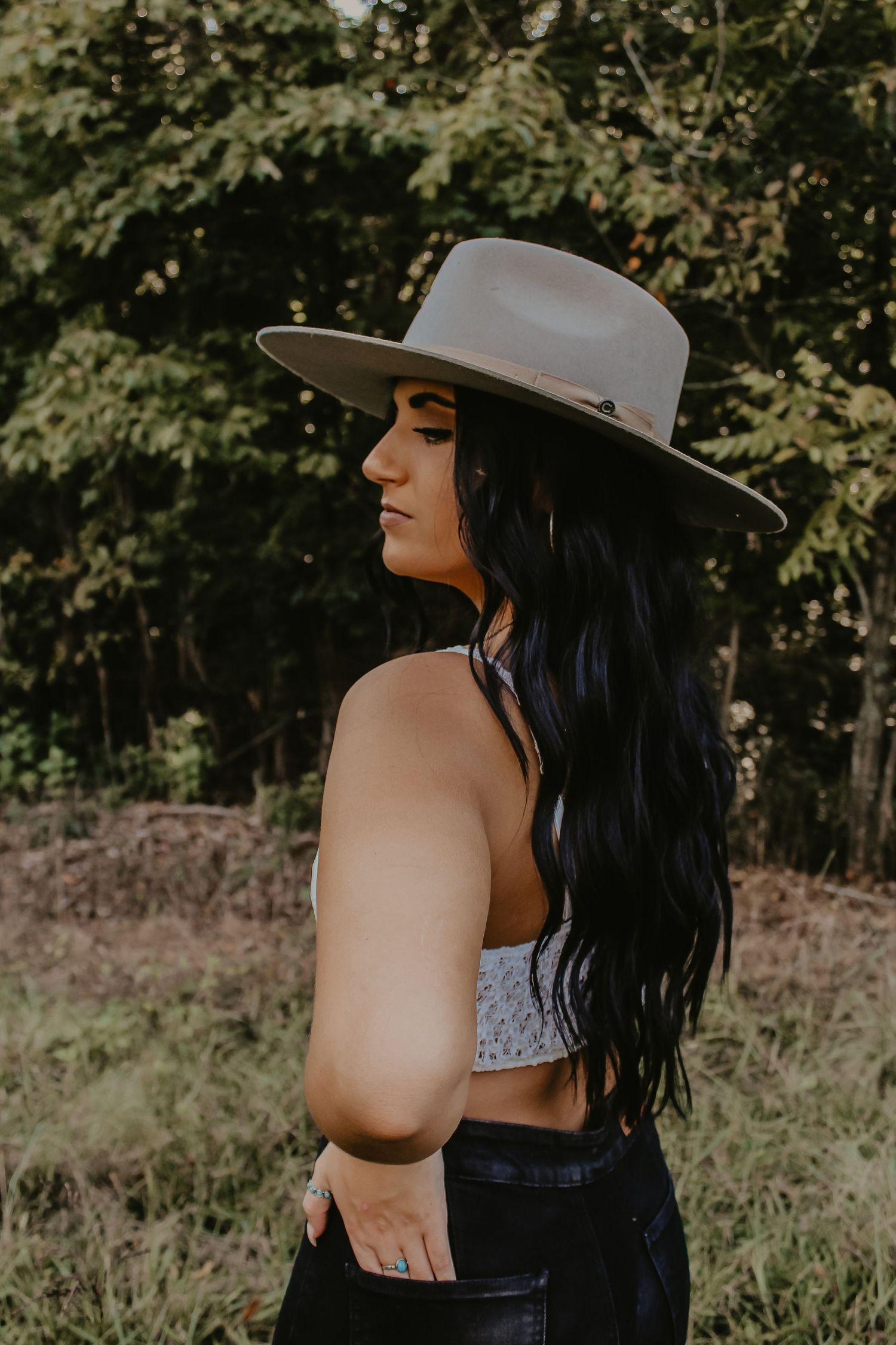 Side profile portrait with gray western hat against natural foliage background.