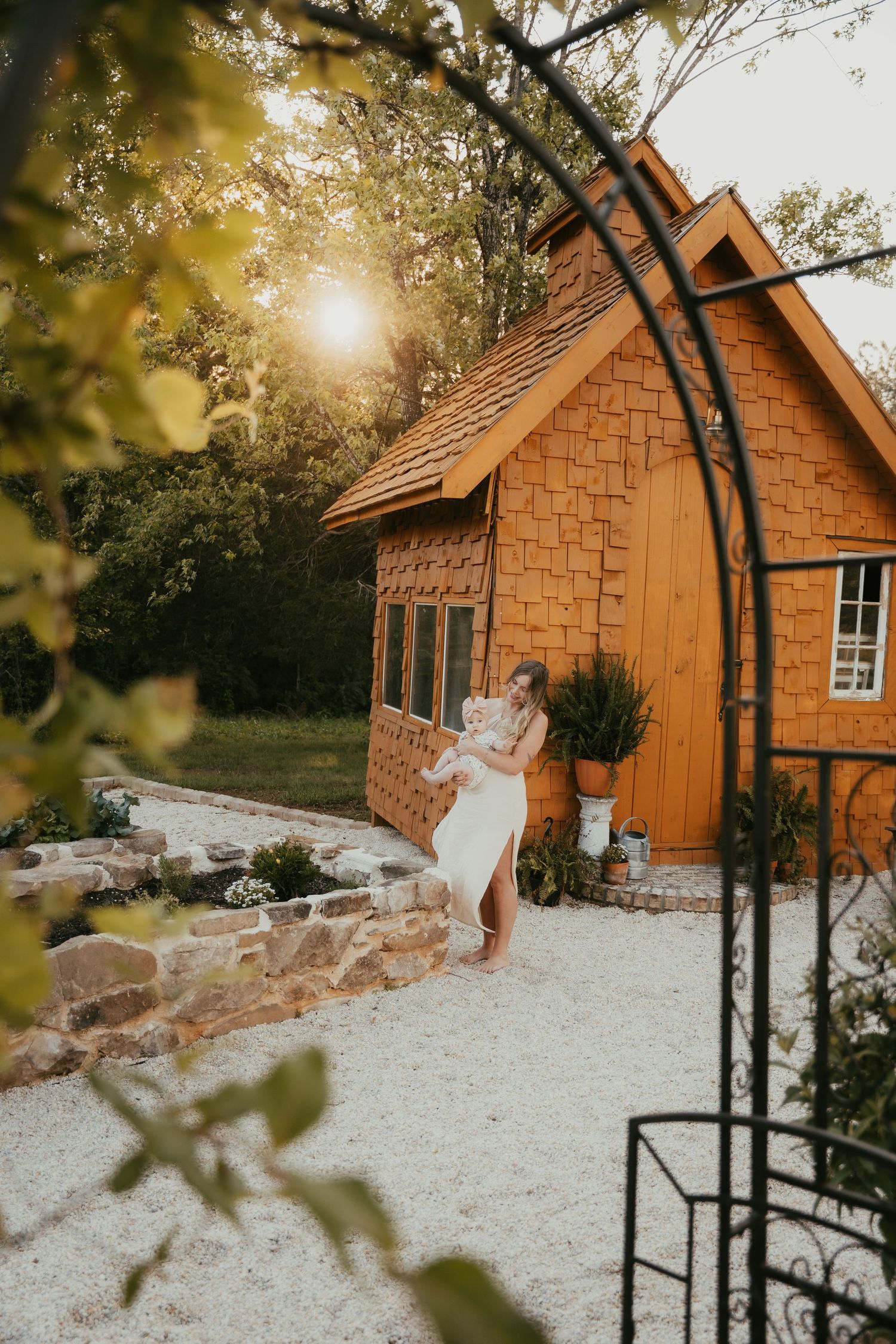 Rustic cedar shake cottage with white gravel path and garden arch at sunset.