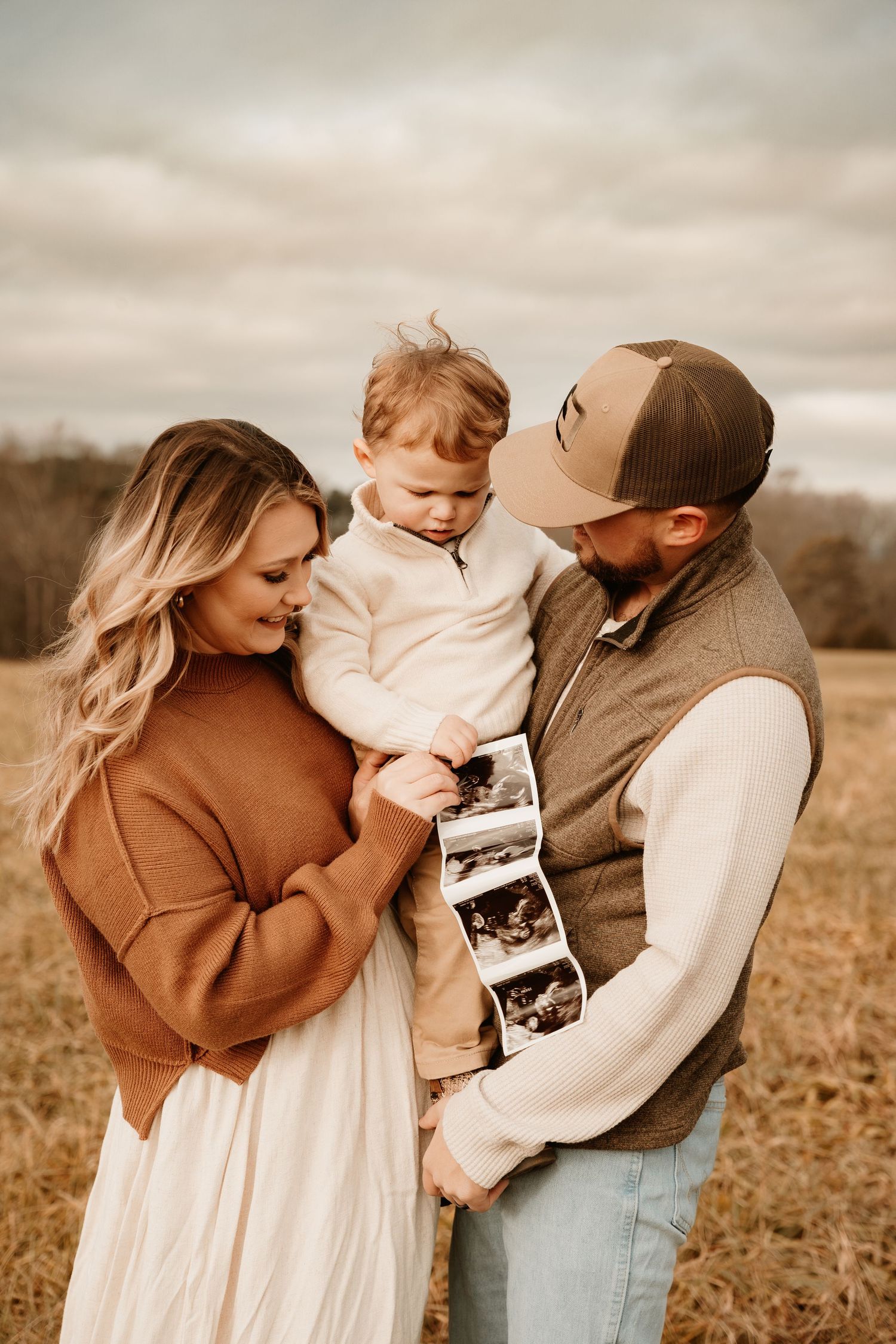 Family shares tender moments together in a rustic field during golden hour photography session.