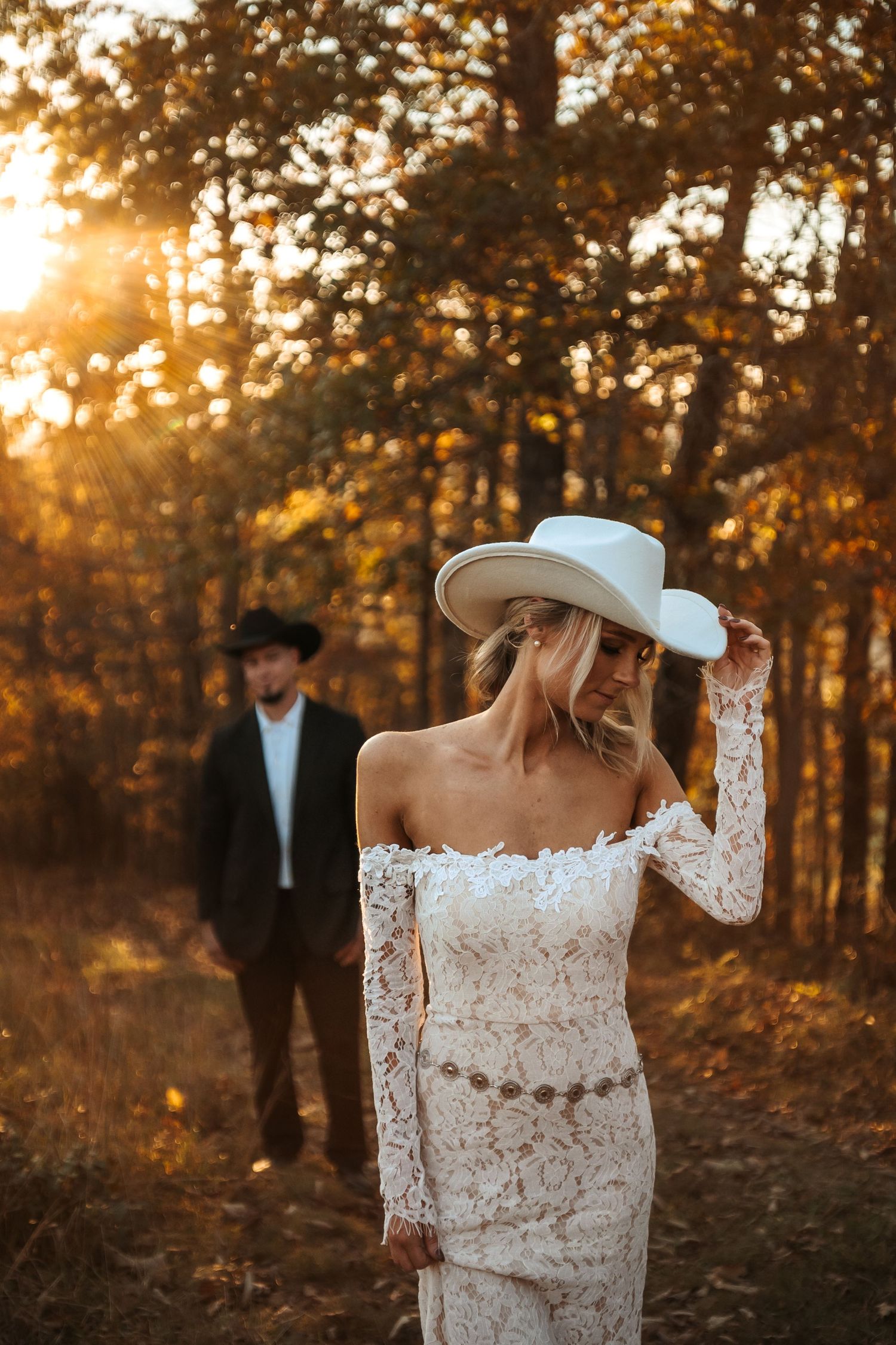 Bride in lace dress and cowboy hat during golden hour forest wedding session.