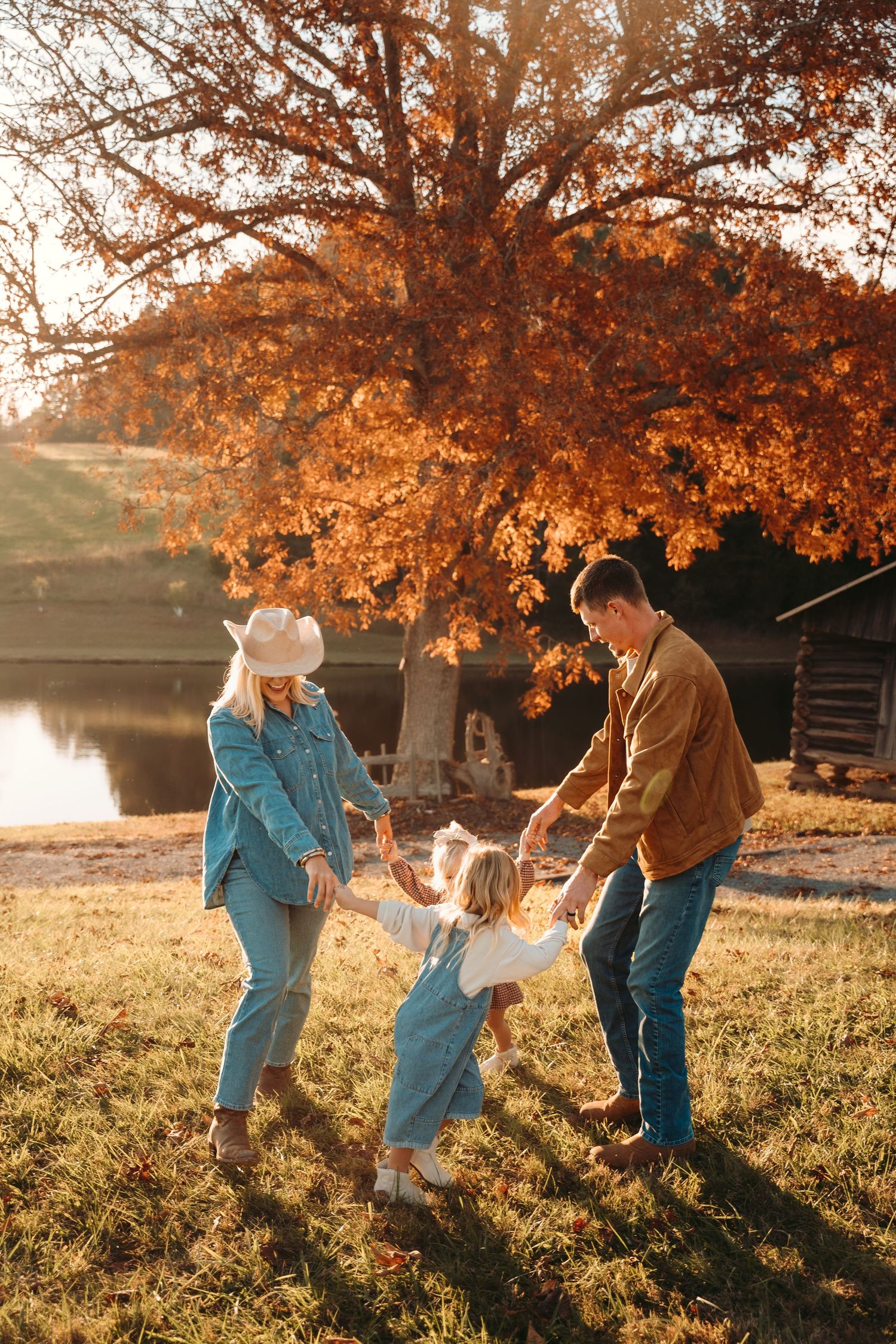 Family playing together under autumn trees during golden hour in a park setting.