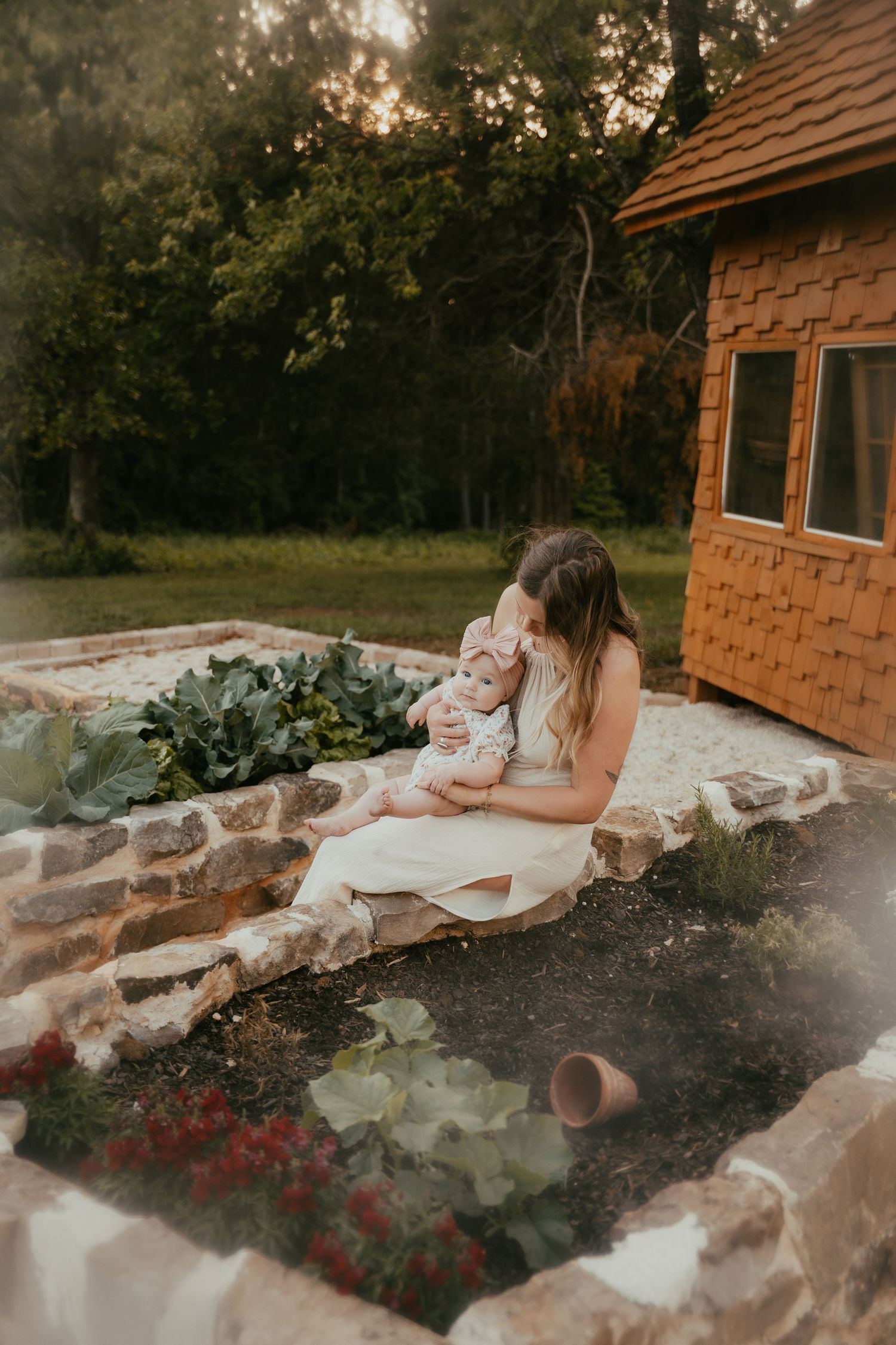 Woman sitting on stone wall with garden pond at sunset near cottage.