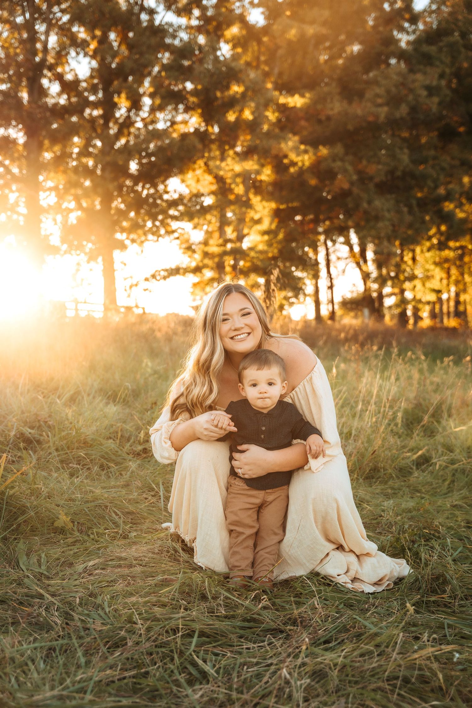 Golden hour family portraits in field with warm sunlight filtering through autumn trees.