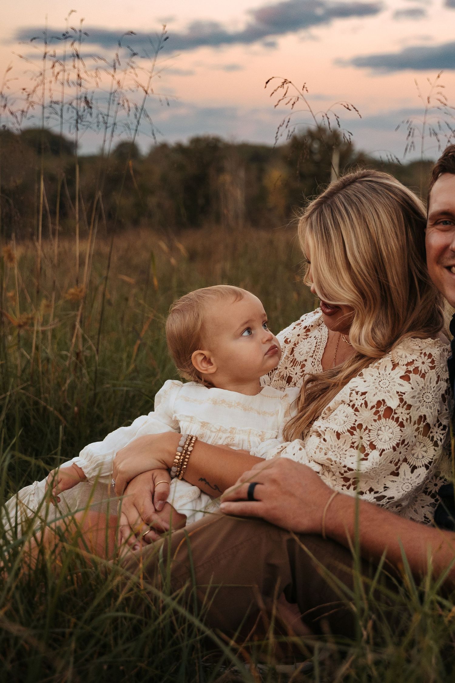 Family lying together in tall grass during golden hour sunset photoshoot.