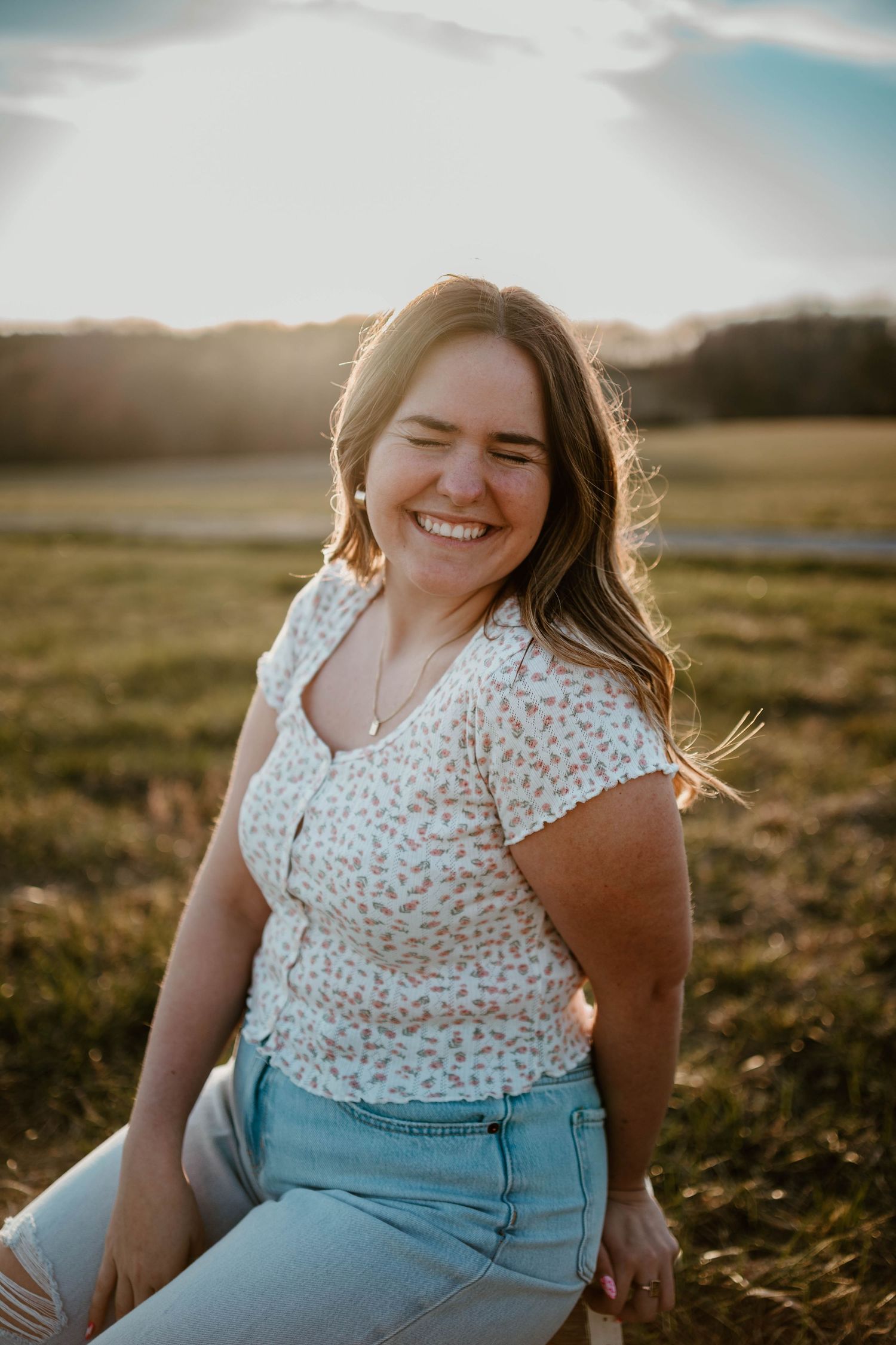 Candid sunset portrait of someone laughing while sitting in a grassy field.