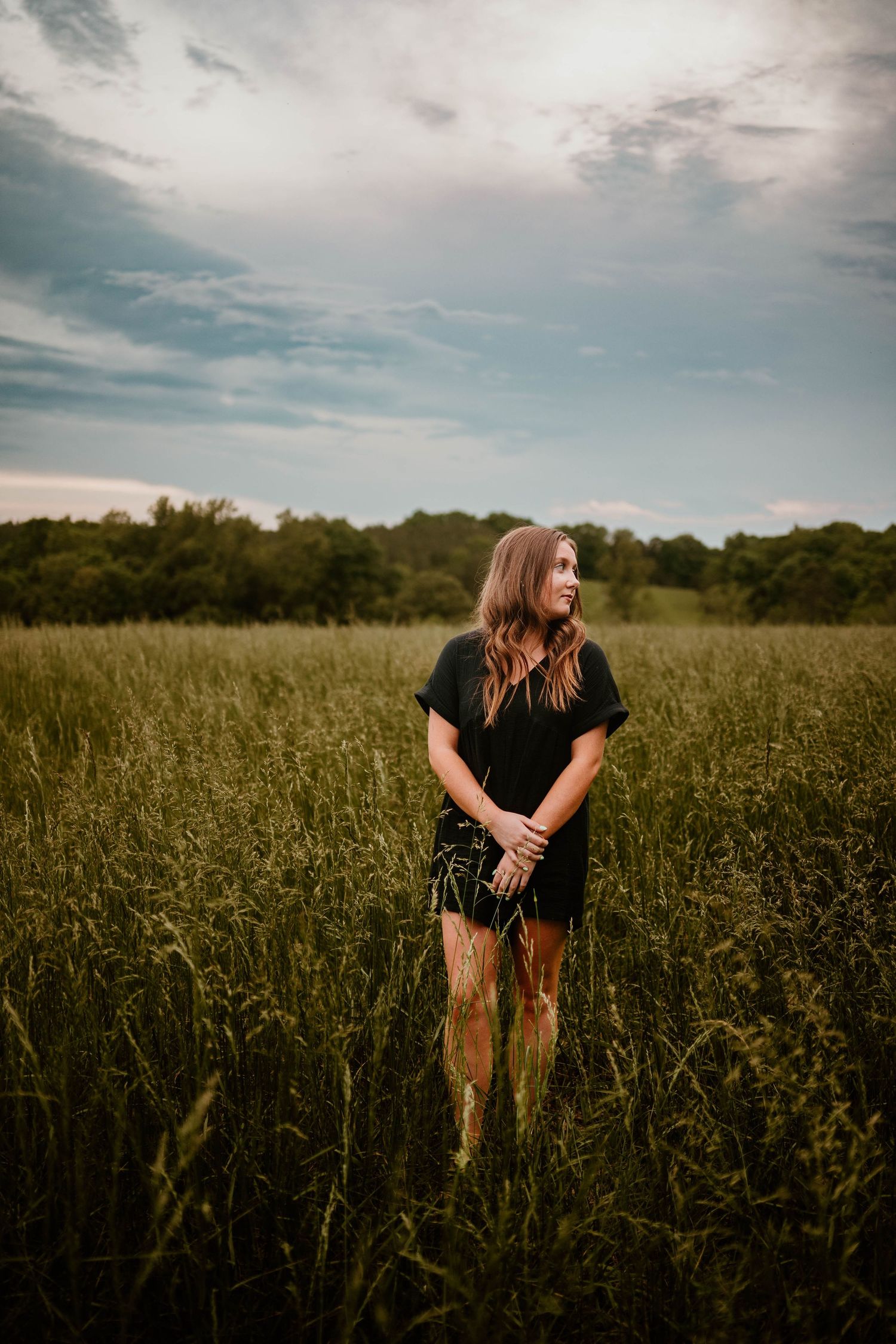 Dramatic cloudy sky sets mood for portrait session in tall grass field.
