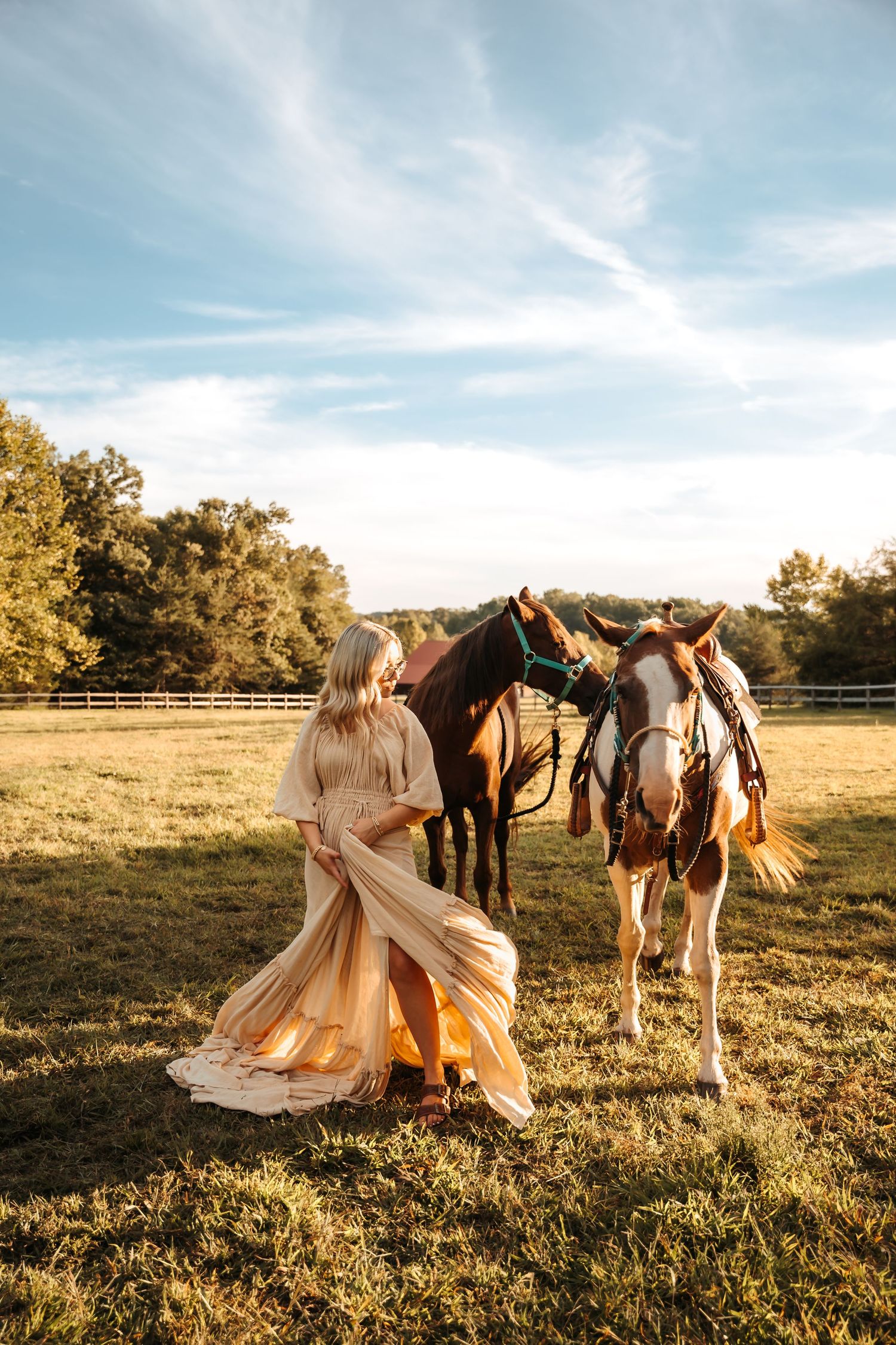 A flowing cream dress twirls in a sunlit field with horses grazing in the background.