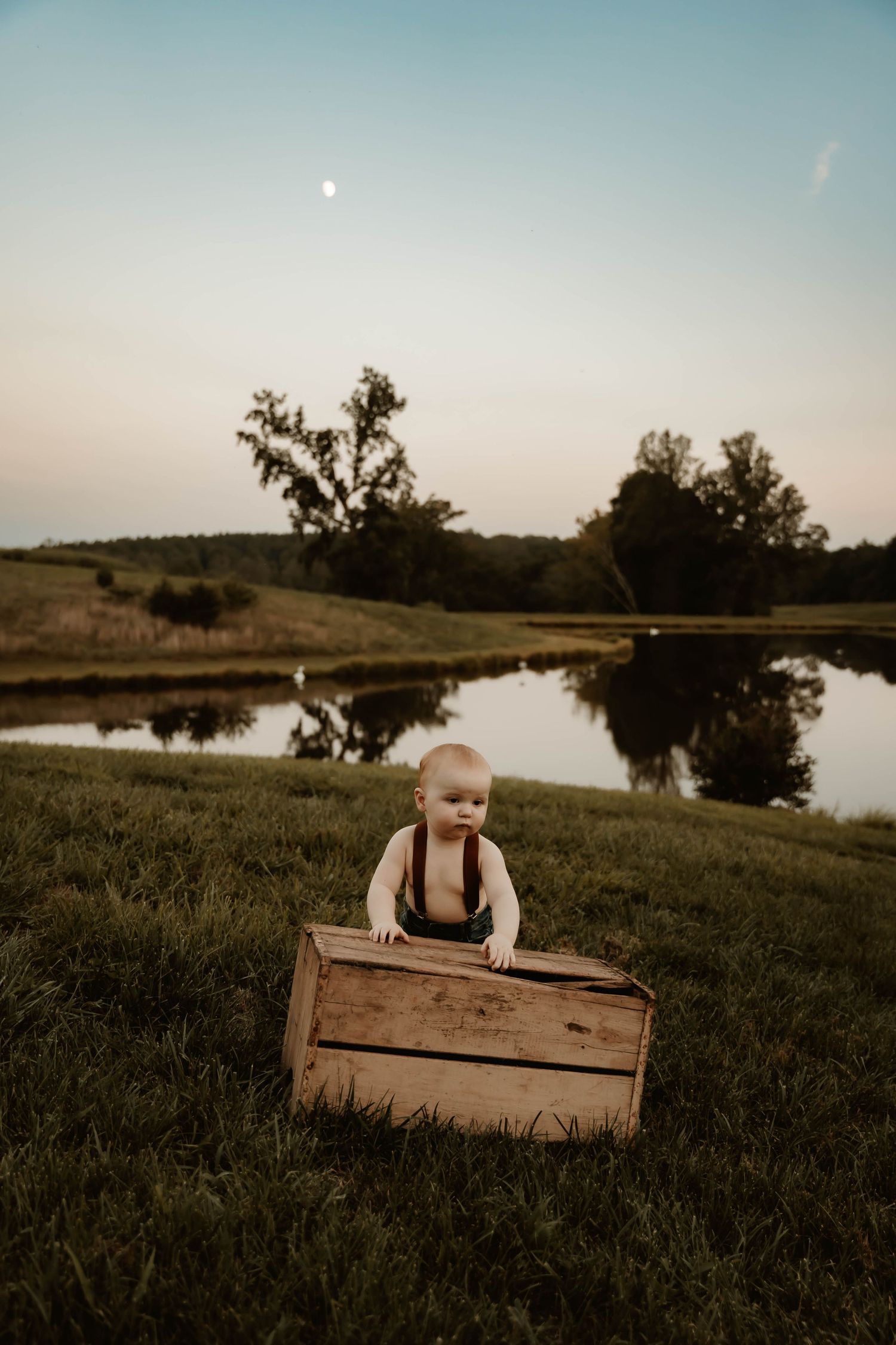 Rustic wooden crates sit in a grassy field beside a tranquil pond at dusk.