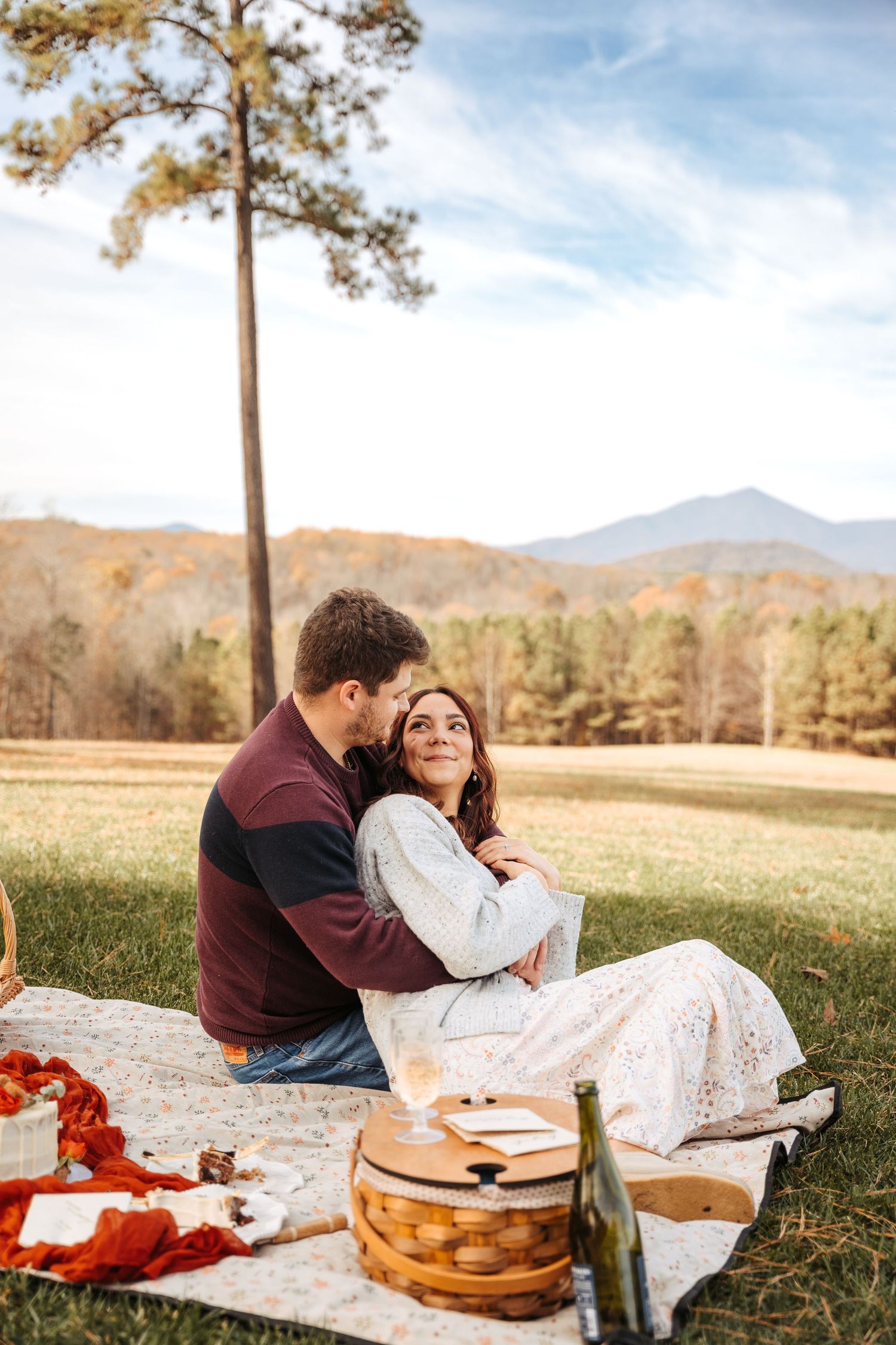 A romantic picnic scene with mountains and autumn trees in the background.