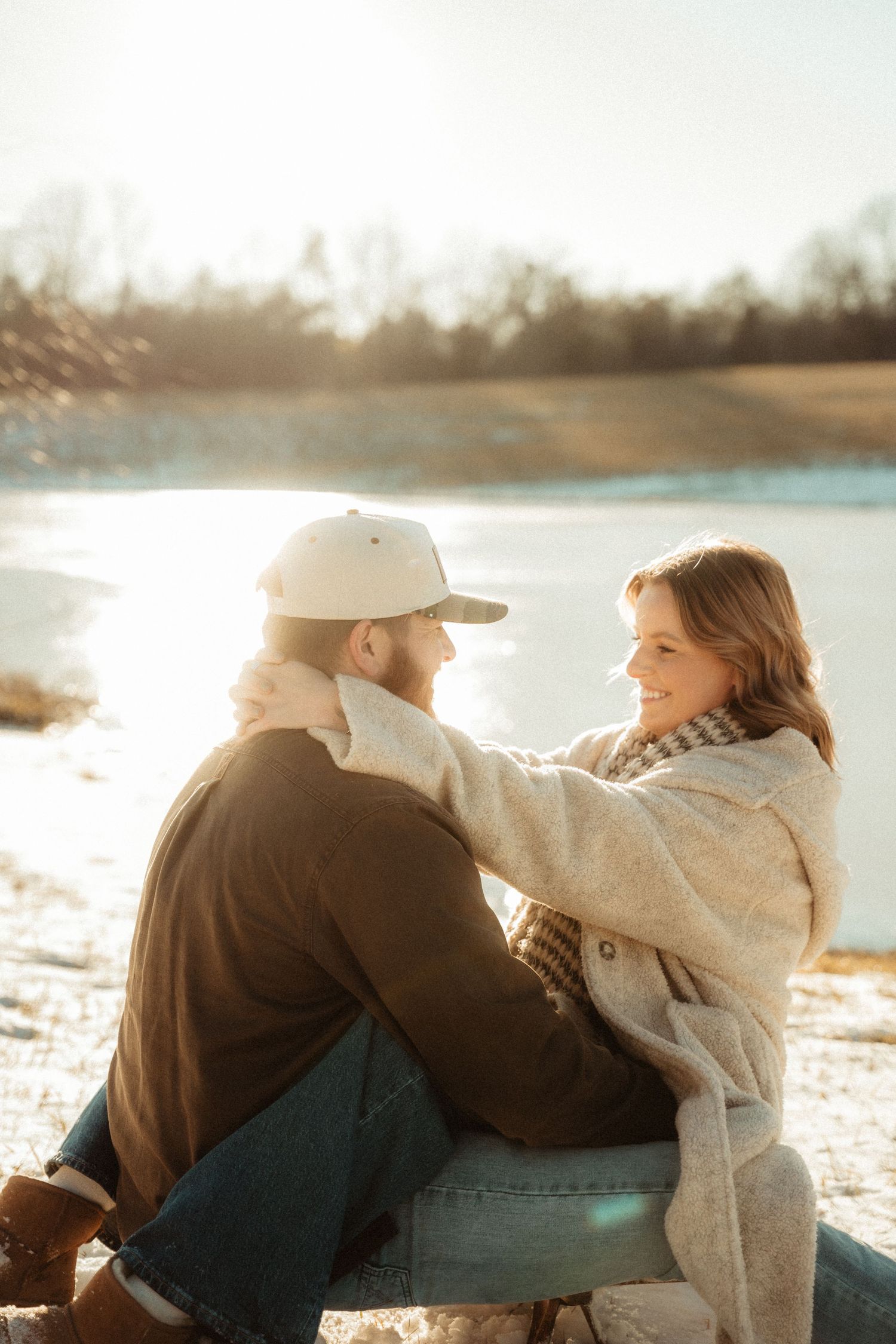 A couple shares a tender moment by a lake during winter sunset.