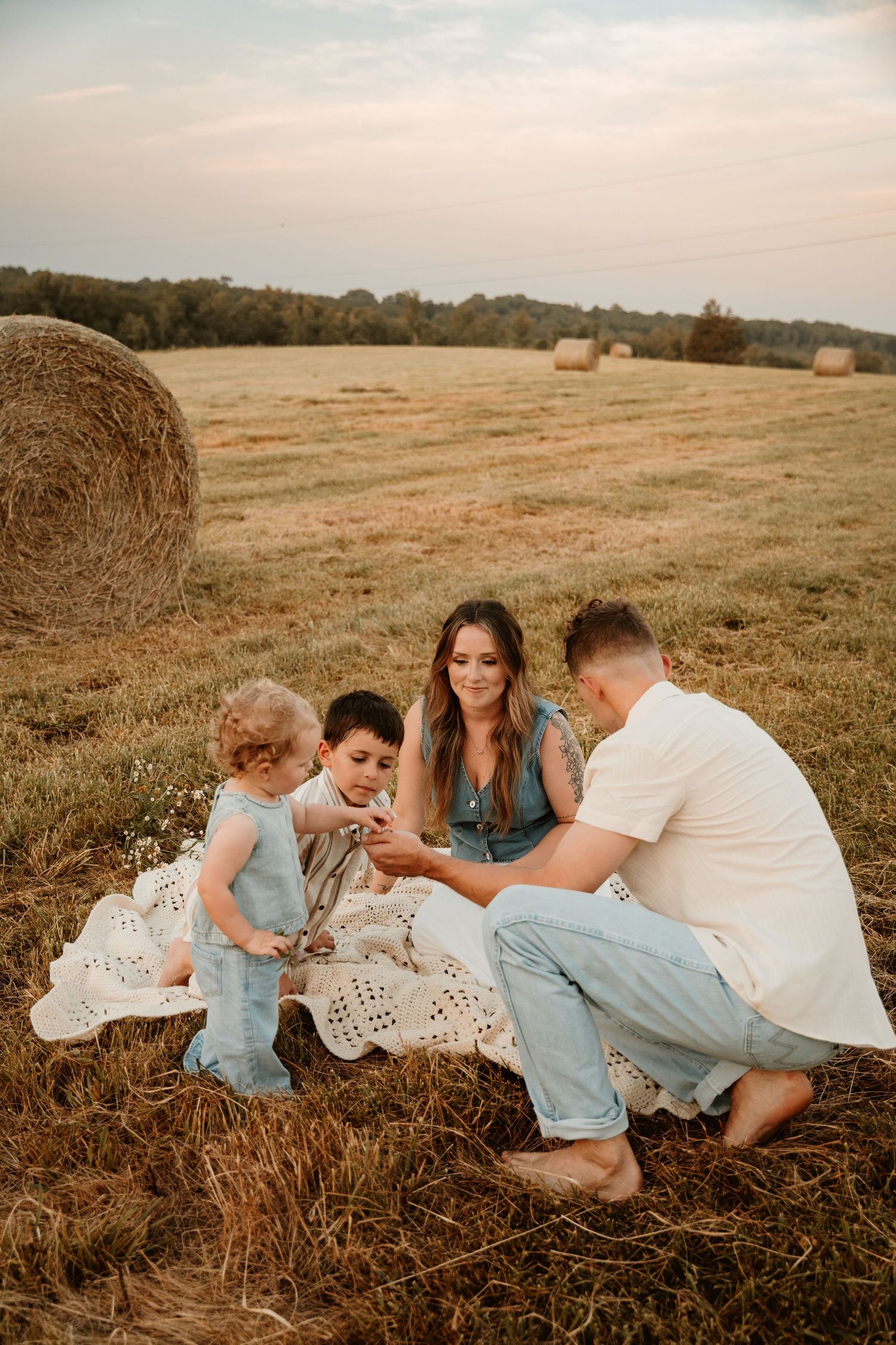 Family relaxing together on hay bales in golden summer field at sunset.
