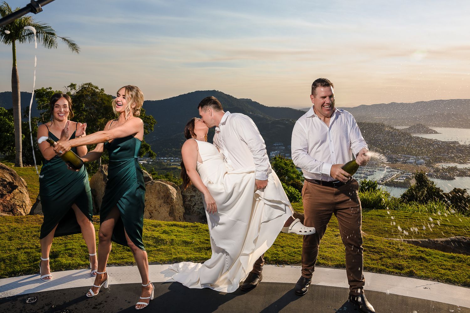 Wedding party poses playfully for photos with mountain and ocean views in background.